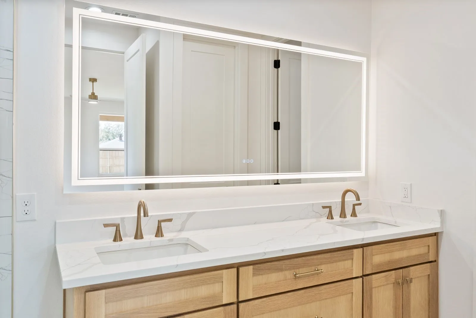 Dual vanity with light wood-finish cabinetry, integrated sinks, and brushed gold fixtures