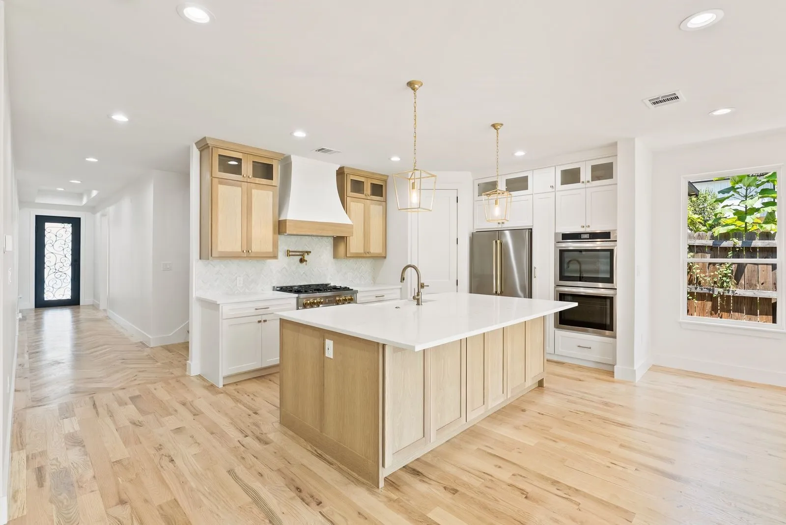 Gourmet kitchen featuring a central island with sink, stainless steel appliances, custom cabinetry, and wood-finish flooring