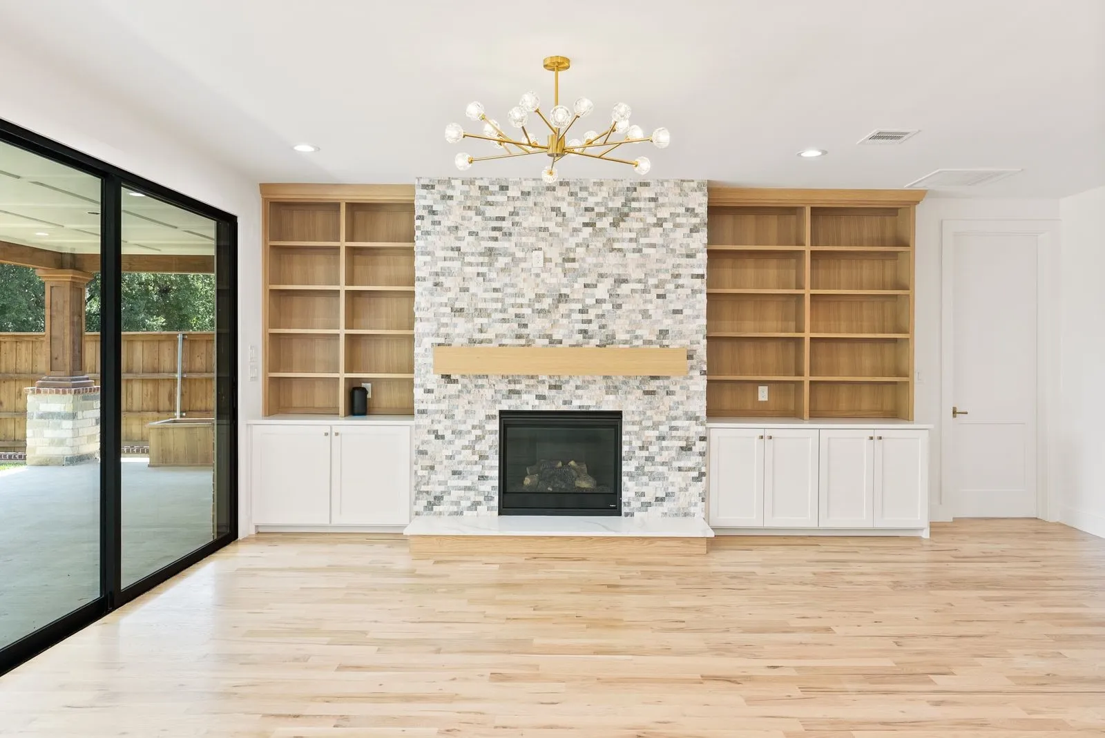 Light wood-finish flooring, built-in shelving, white cabinetry, integrated fireplace with a tile surround, and a modern chandelier