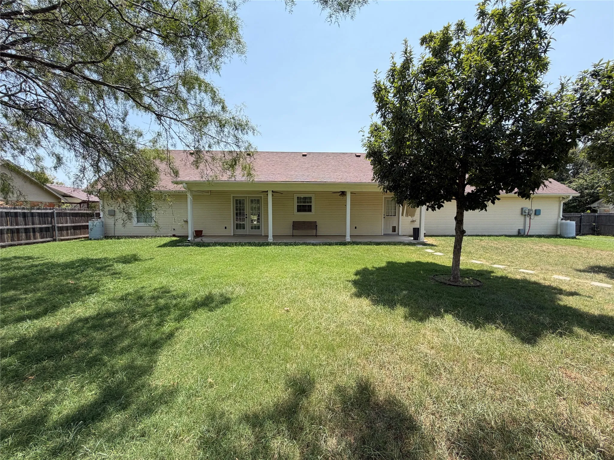Expansive backyard with a covered patio, double French doors, a manicured lawn, and mature trees