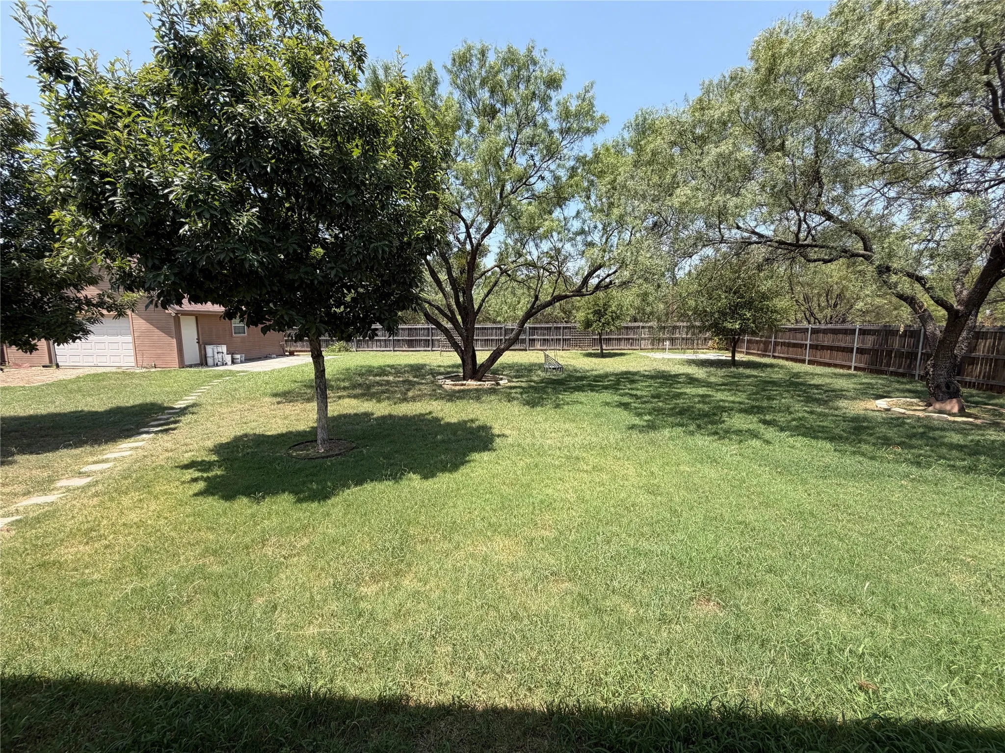 Expansive backyard featuring a lush lawn, mature trees, and a full perimeter fence