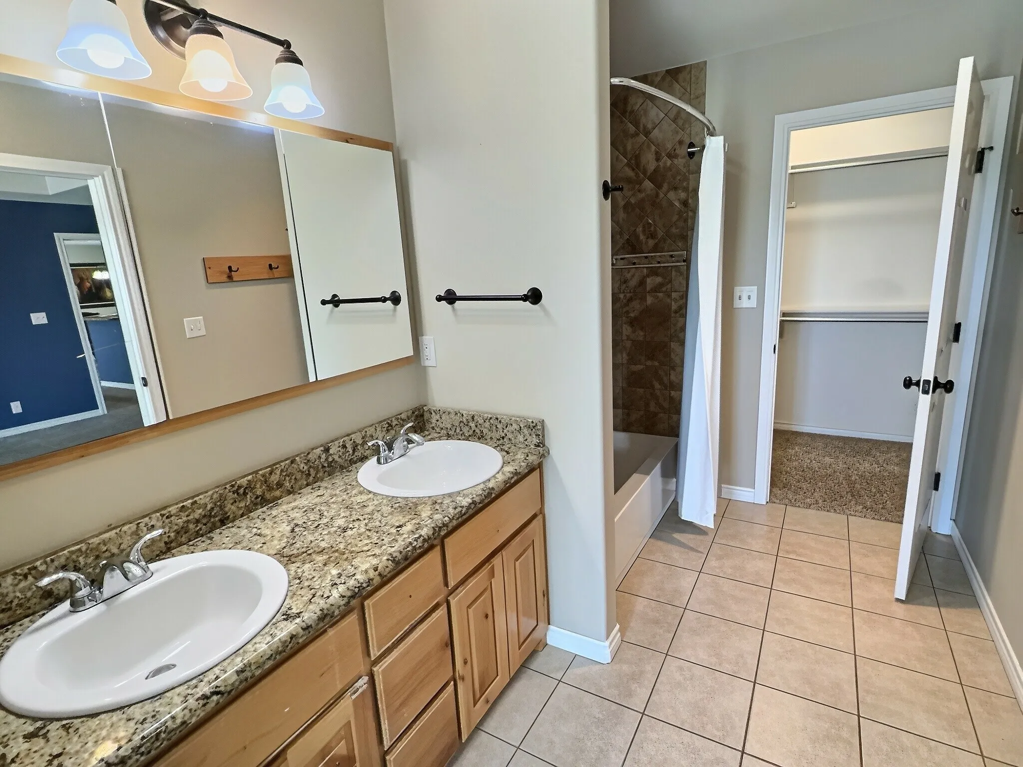 Dual vanity with granite-style countertop, tile flooring, and integrated shower/tub combination with tiled surround