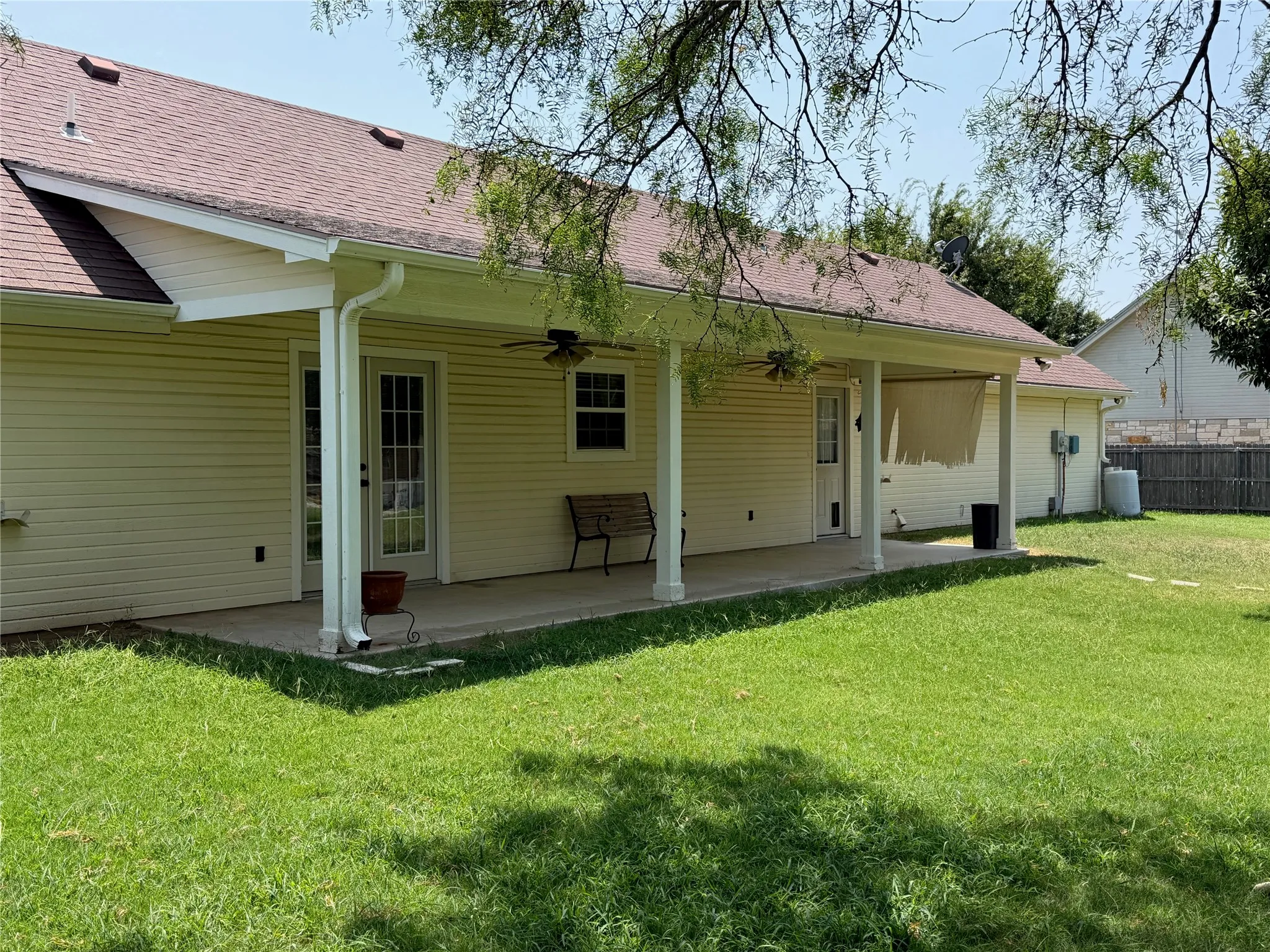 Expansive covered patio with multiple ceiling fans, light-toned siding, and a large grassy area