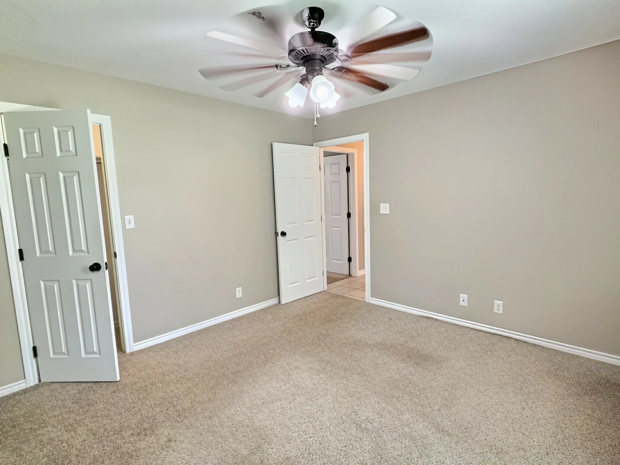 Neutral tone walls, carpeted flooring, and a ceiling fan with integrated lighting