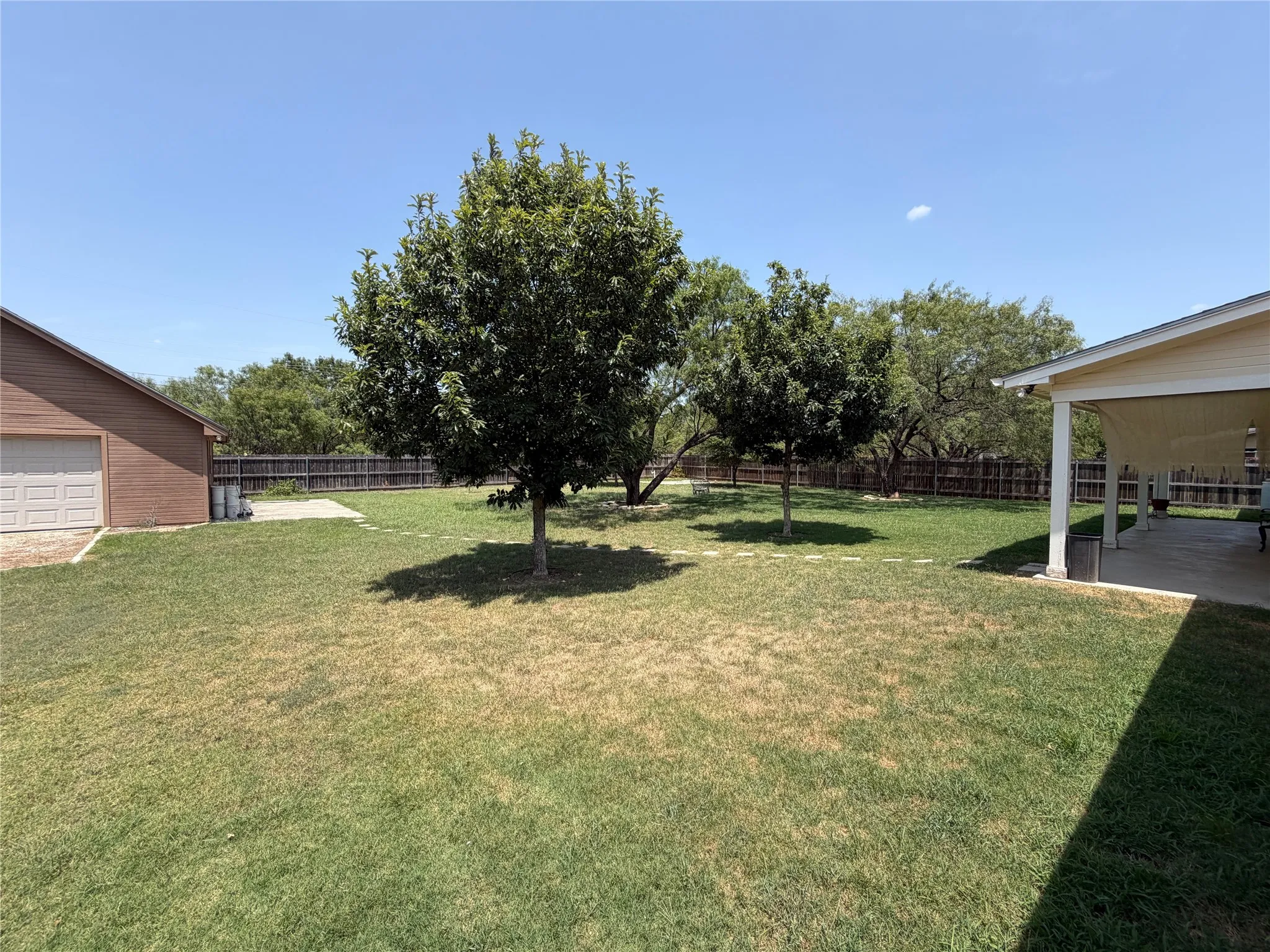 Expansive grassy area with mature trees, a covered patio, and a separate structure featuring a garage door