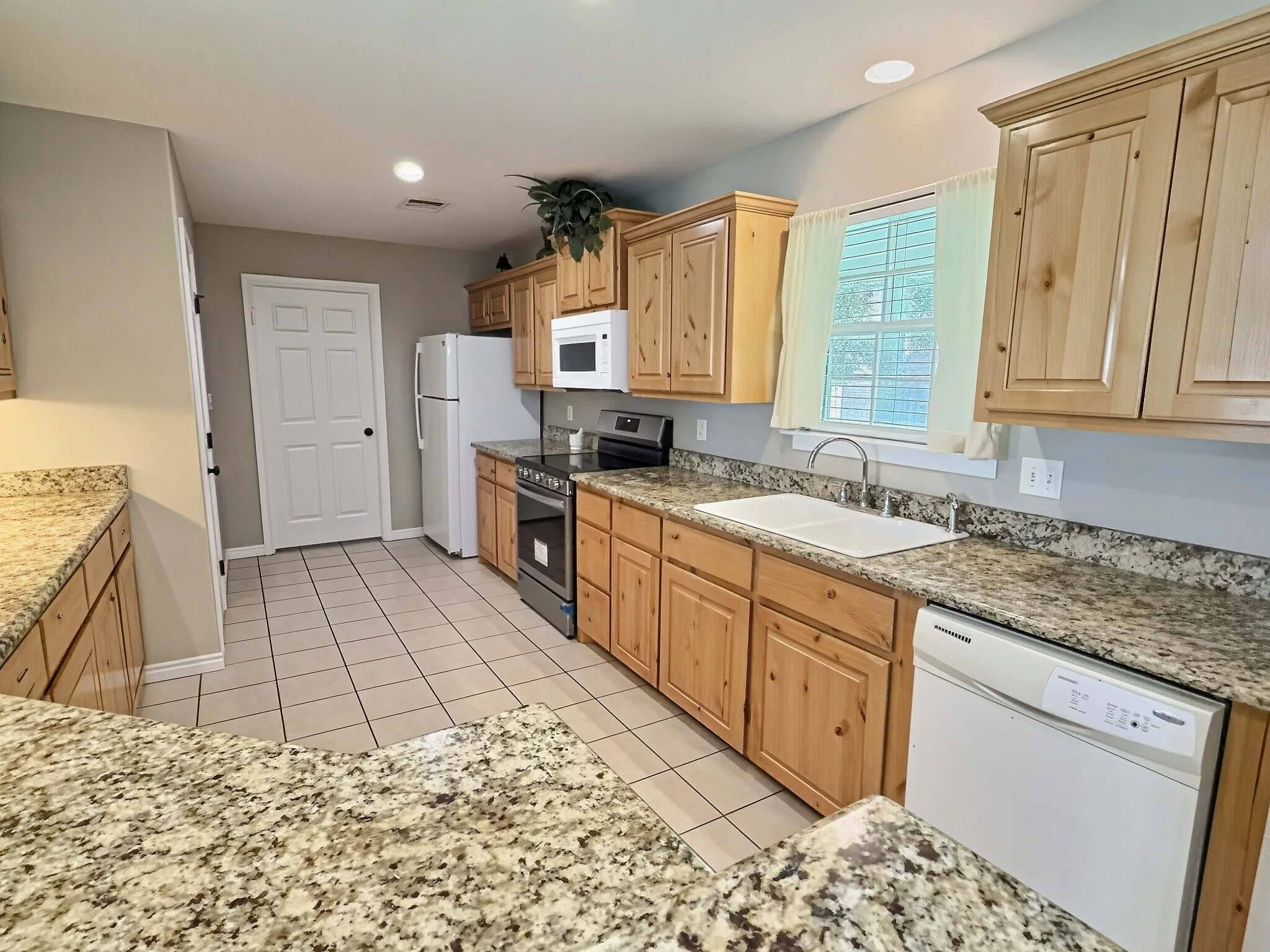 Kitchen featuring light wood cabinetry, stone-finish countertops, tile flooring, and white appliances