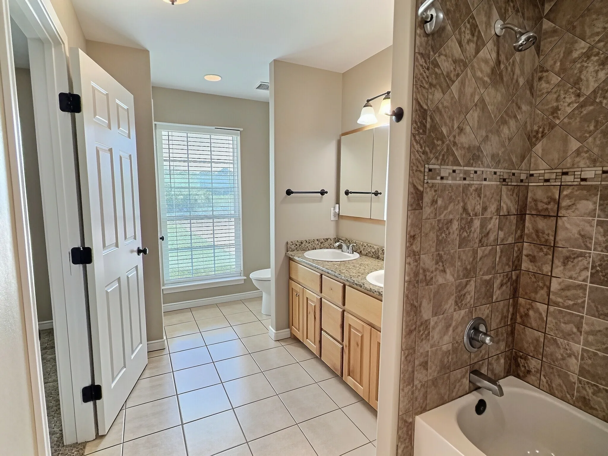Double vanity with sinks, wood cabinetry, tile flooring, and a tiled shower-over-tub combination