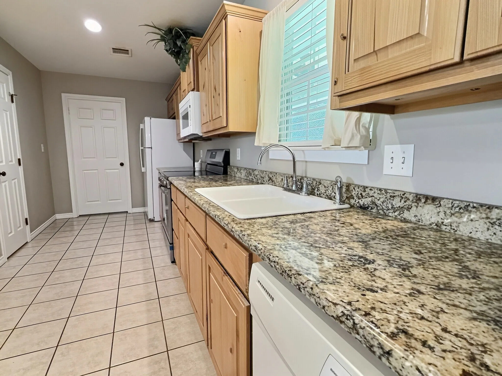 Kitchen featuring light wood cabinetry, stone countertops, a stainless steel faucet, and tile flooring