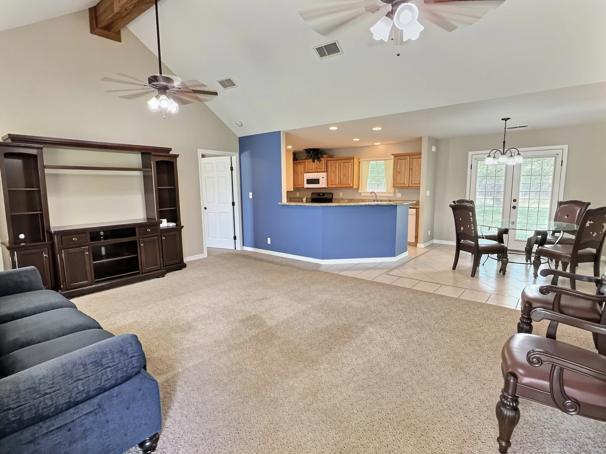 Vaulted ceiling with exposed wood beam, kitchen with wood cabinetry and stone countertops, tiled dining area, and French patio doors
