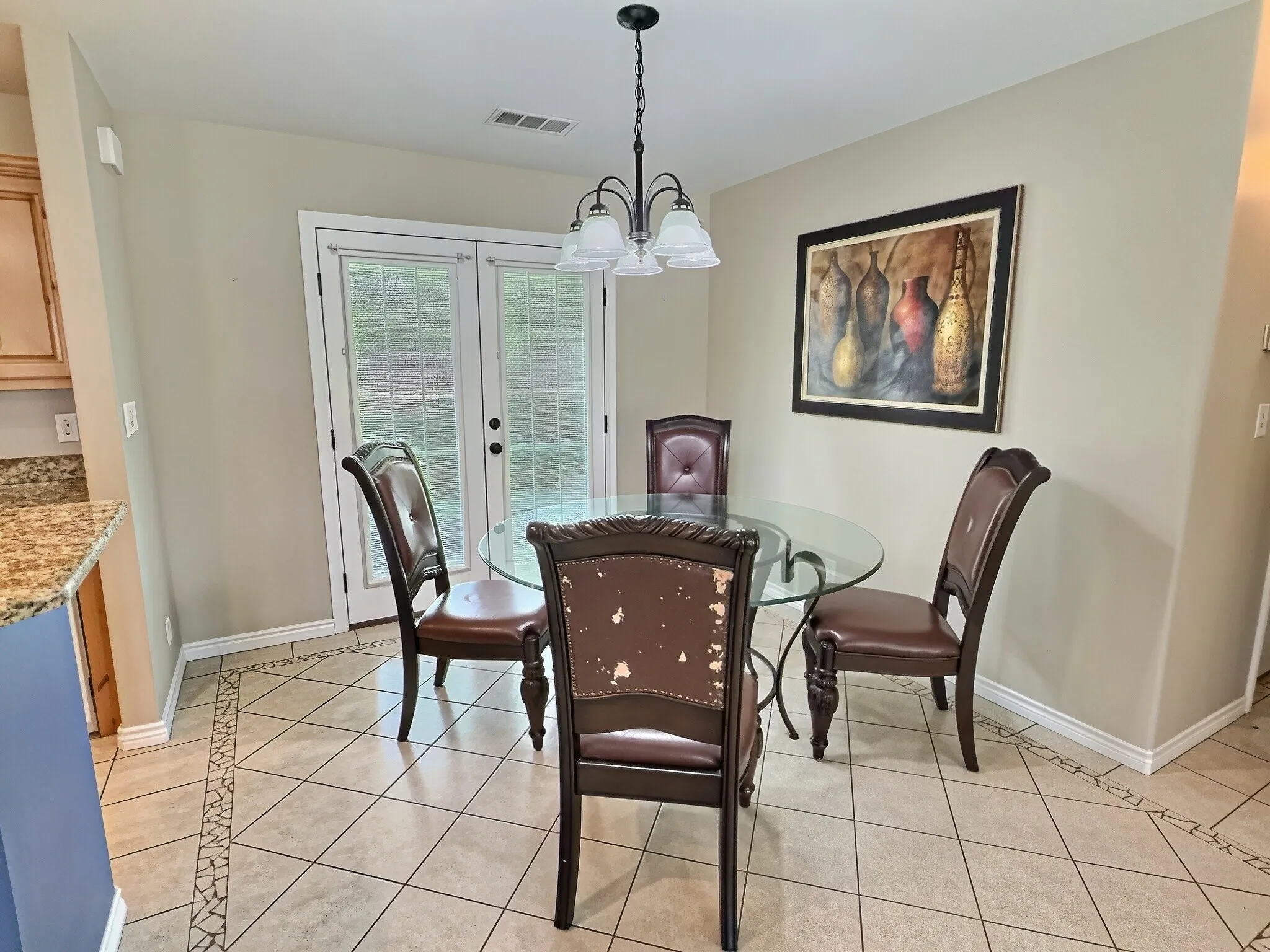 French doors with frosted glass panels, tile flooring with decorative inlay, overhead chandelier lighting, and a granite-finish countertop