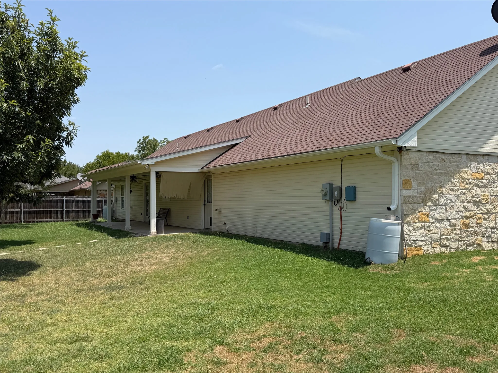 Expansive backyard featuring a covered patio, wood fencing, and a combination of siding and stone exterior