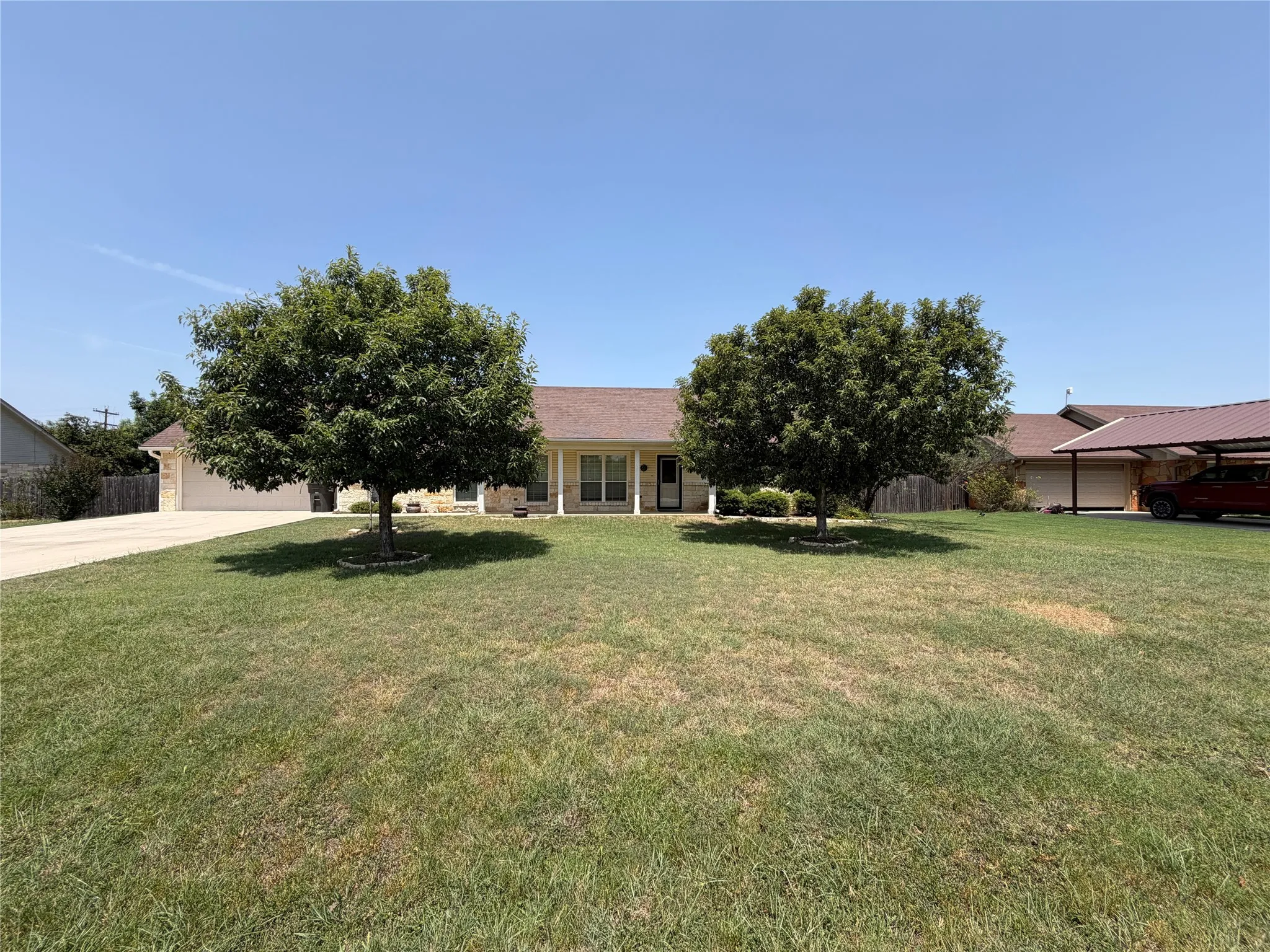 Spacious residential property featuring a single-story brick and stone exterior with a pitched roof, set on an expansive manicured lawn anchored by two mature shade trees