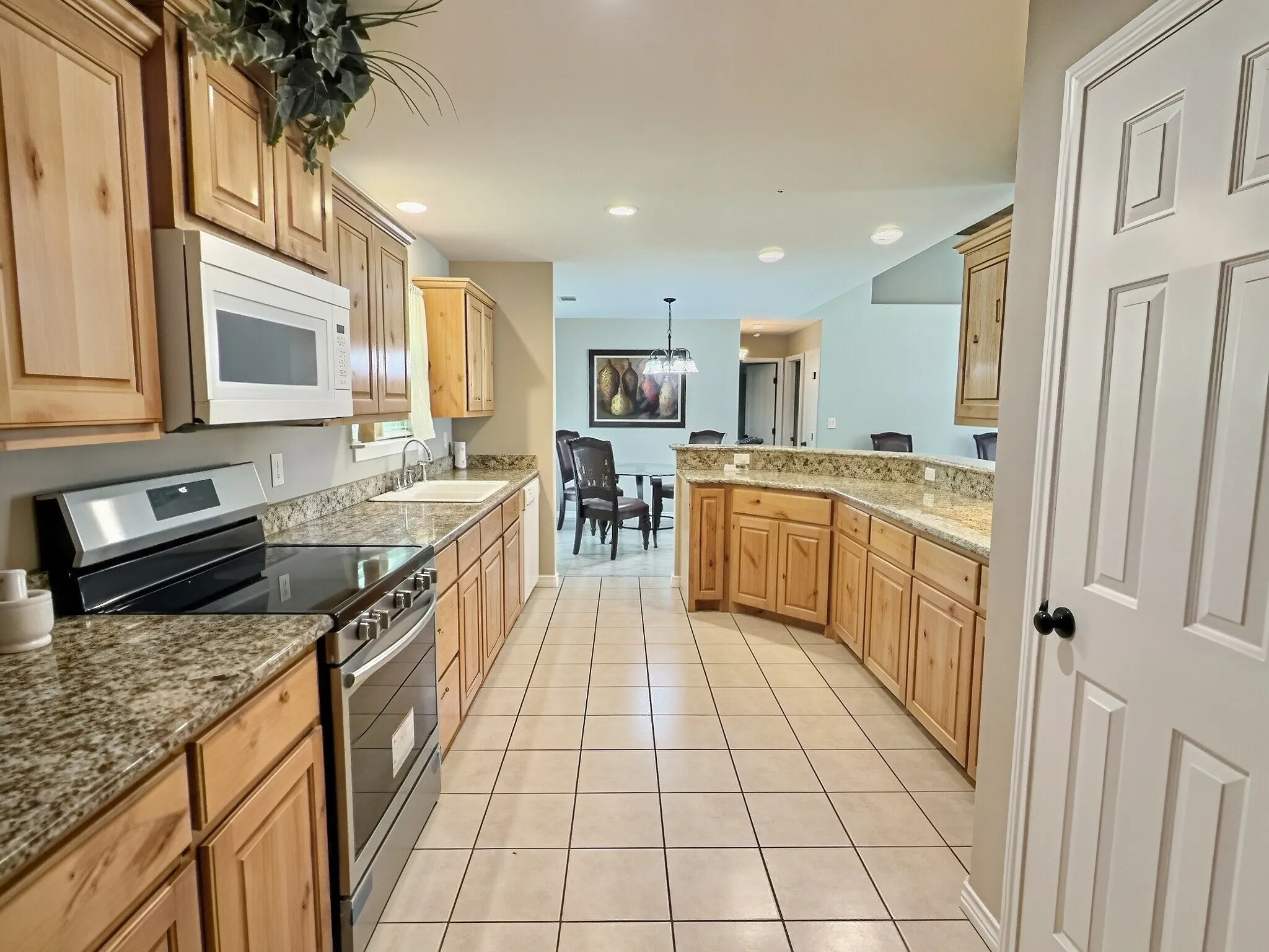 Kitchen featuring wood-finish cabinetry, light-toned countertop, stainless steel appliances, and a tile floor