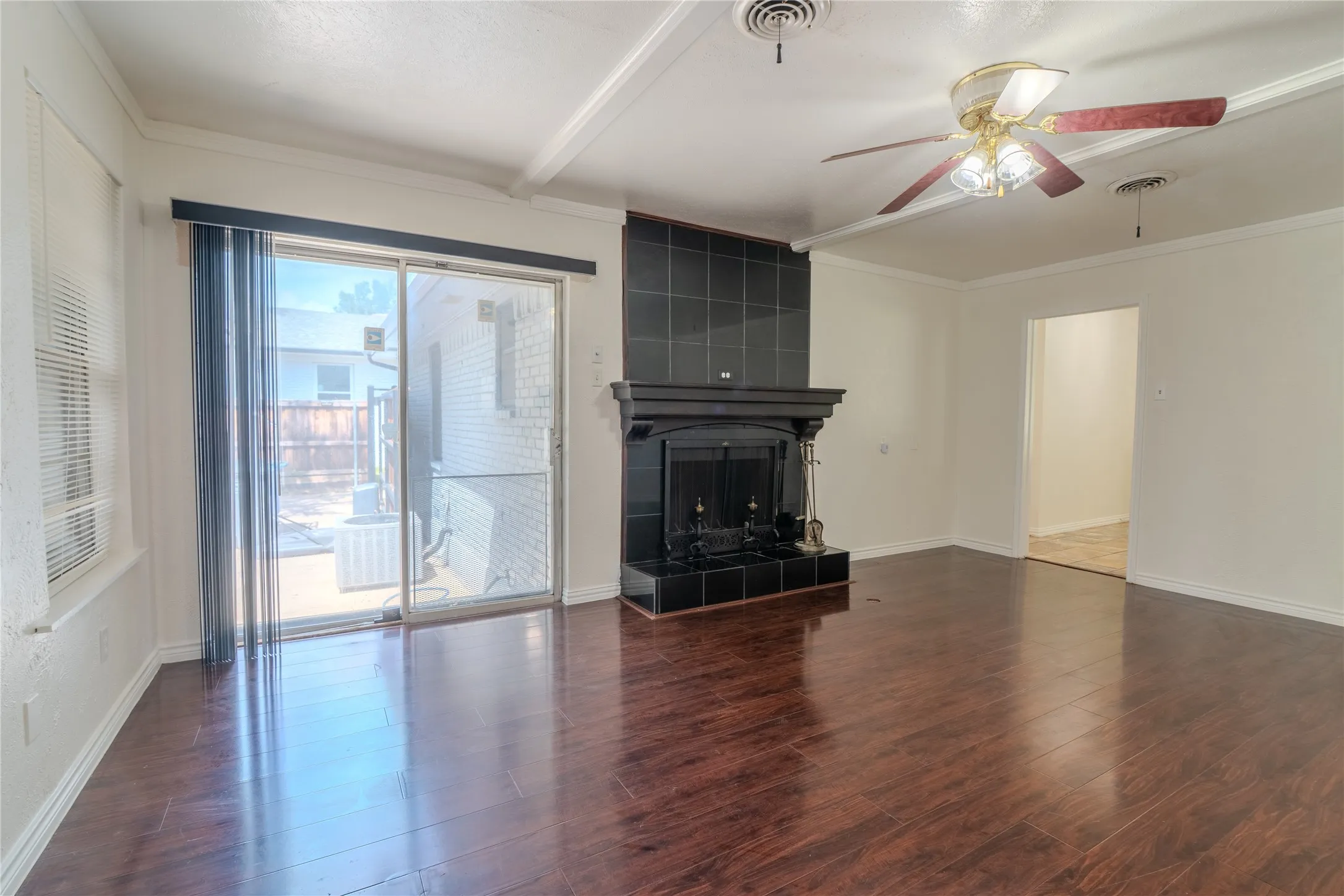 Spacious living area featuring rich wood-finish flooring, a black tile fireplace with mantel, ceiling fan with lighting, and sliding glass doors providing natural light