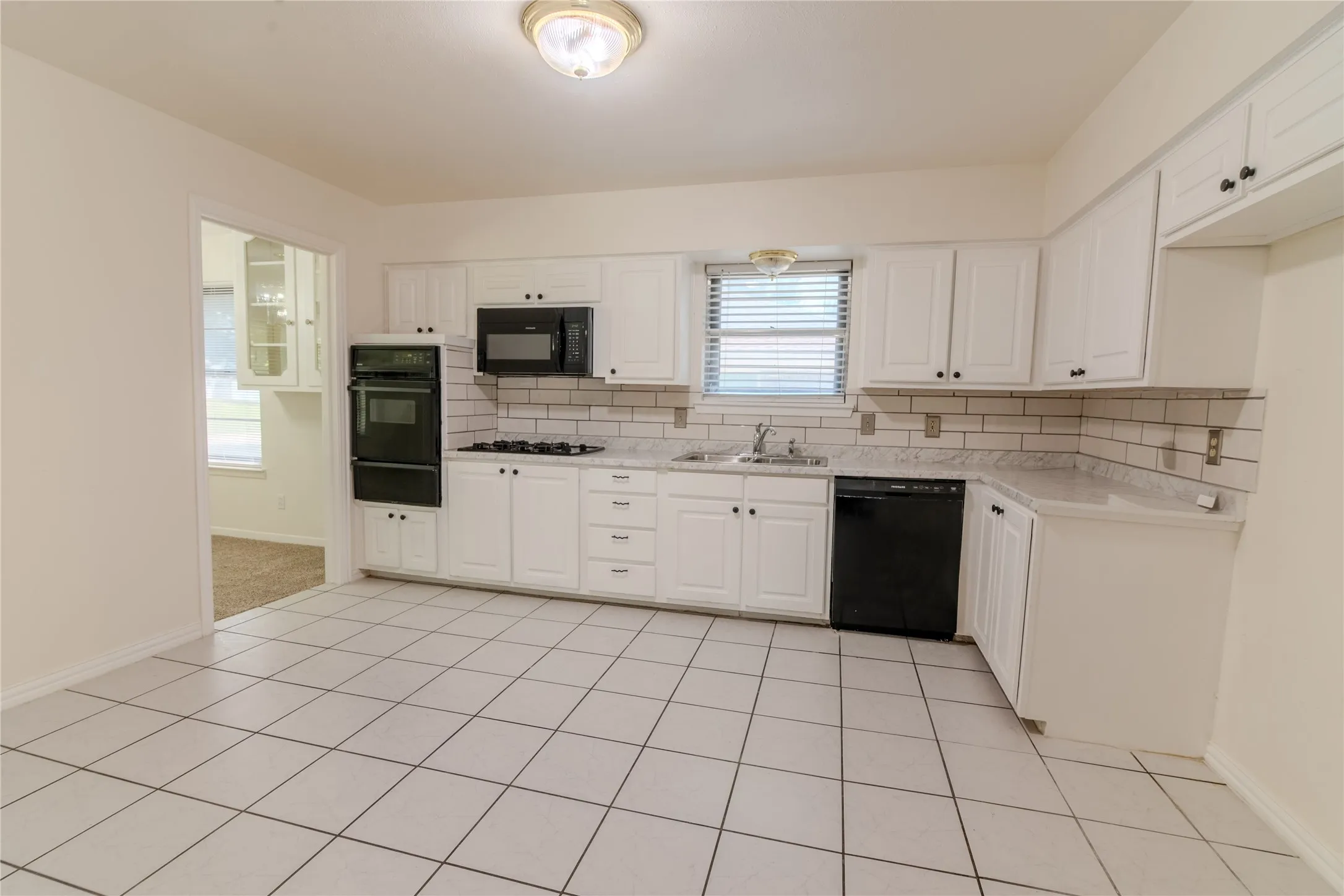 Spacious kitchen featuring white cabinetry with hardware accents, stainless steel appliances including a gas cooktop and built-in microwave, tile countertops, subway tile backsplash, and ceramic tile flooring throughout