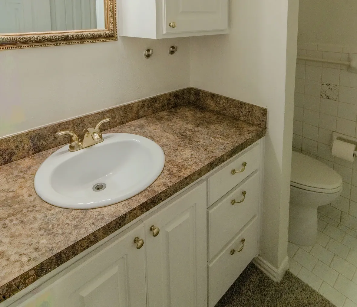 Bathroom vanity featuring a white oval sink, gold-tone faucet, and white cabinetry with gold-tone hardware