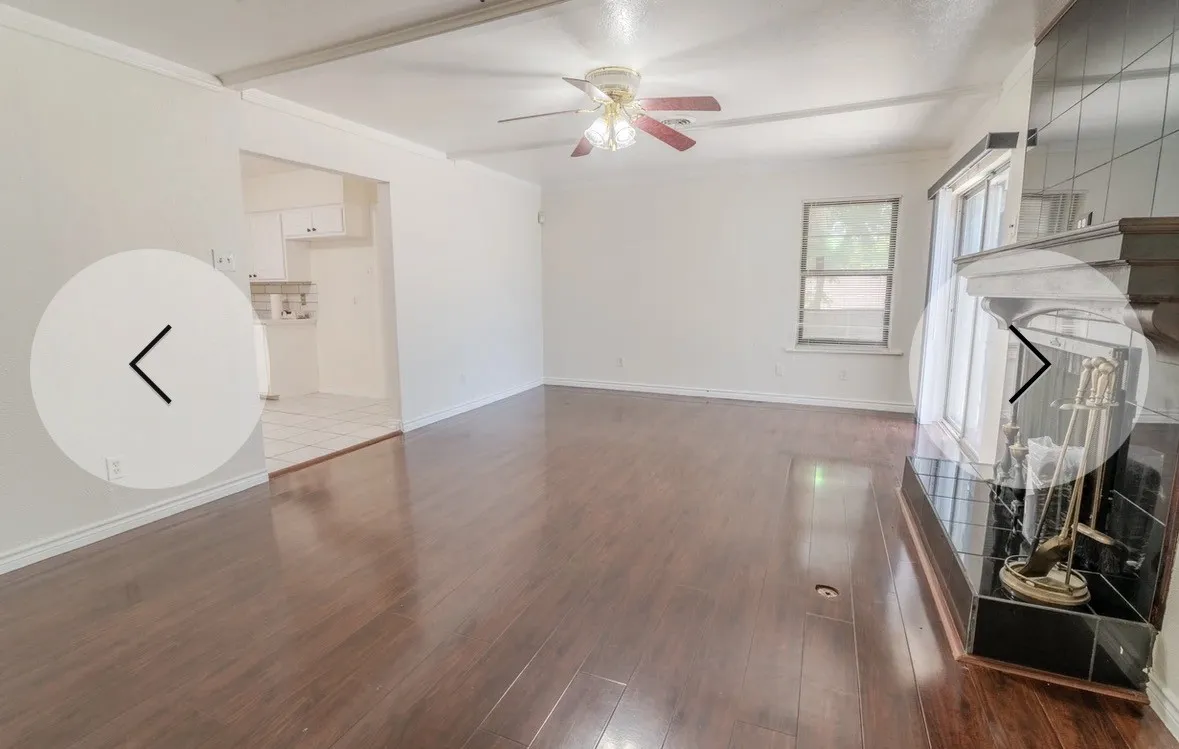 Wood-finish flooring throughout, ceiling fan, and a fireplace with a tiled surround