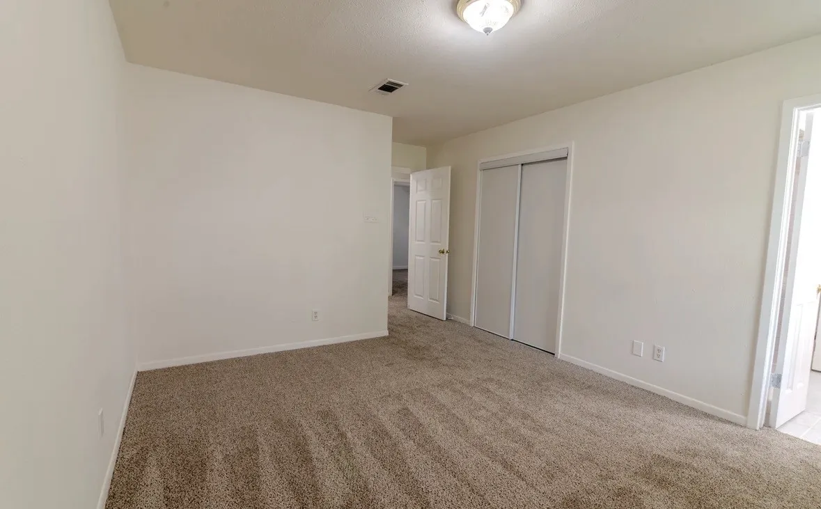 Neutral tone wall paint, textured carpet flooring, ceiling-mounted light fixture, paneled interior door, bi-fold closet doors