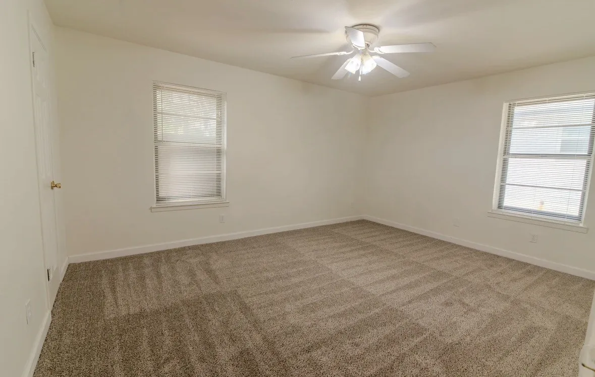 Wall-to-wall carpeting, dual windows with blinds, ceiling fan with integrated lighting, and a white paneled door