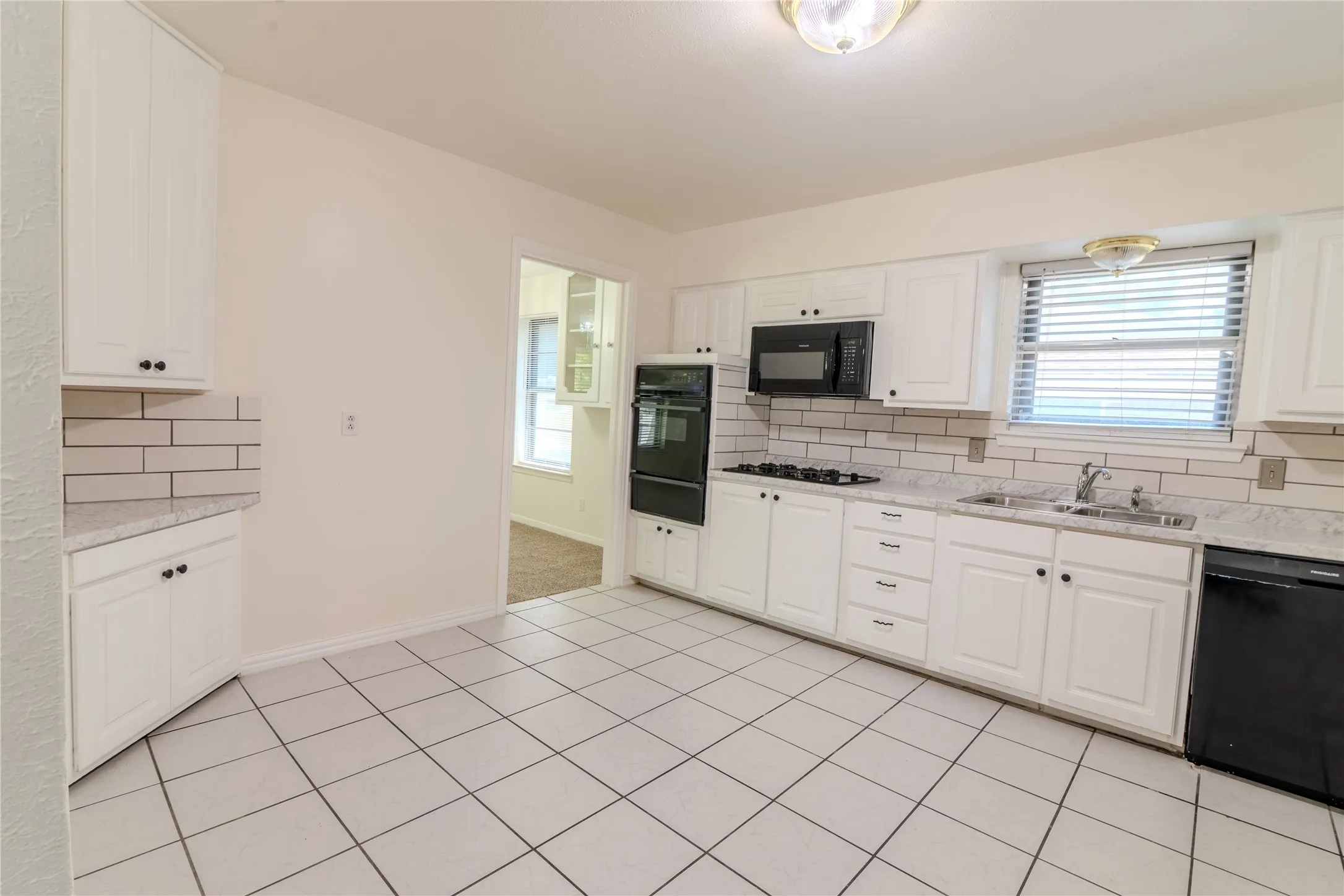 Spacious kitchen featuring white cabinetry, stainless steel appliances, subway tile backsplash, ceramic tile flooring, and ample counter space with a window overlooking the exterior