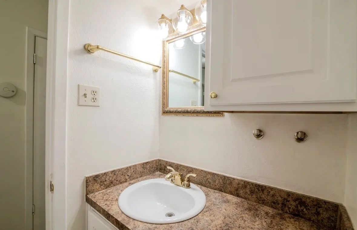 White cabinetry with gold-tone hardware, a drop-in sink, and a patterned countertop