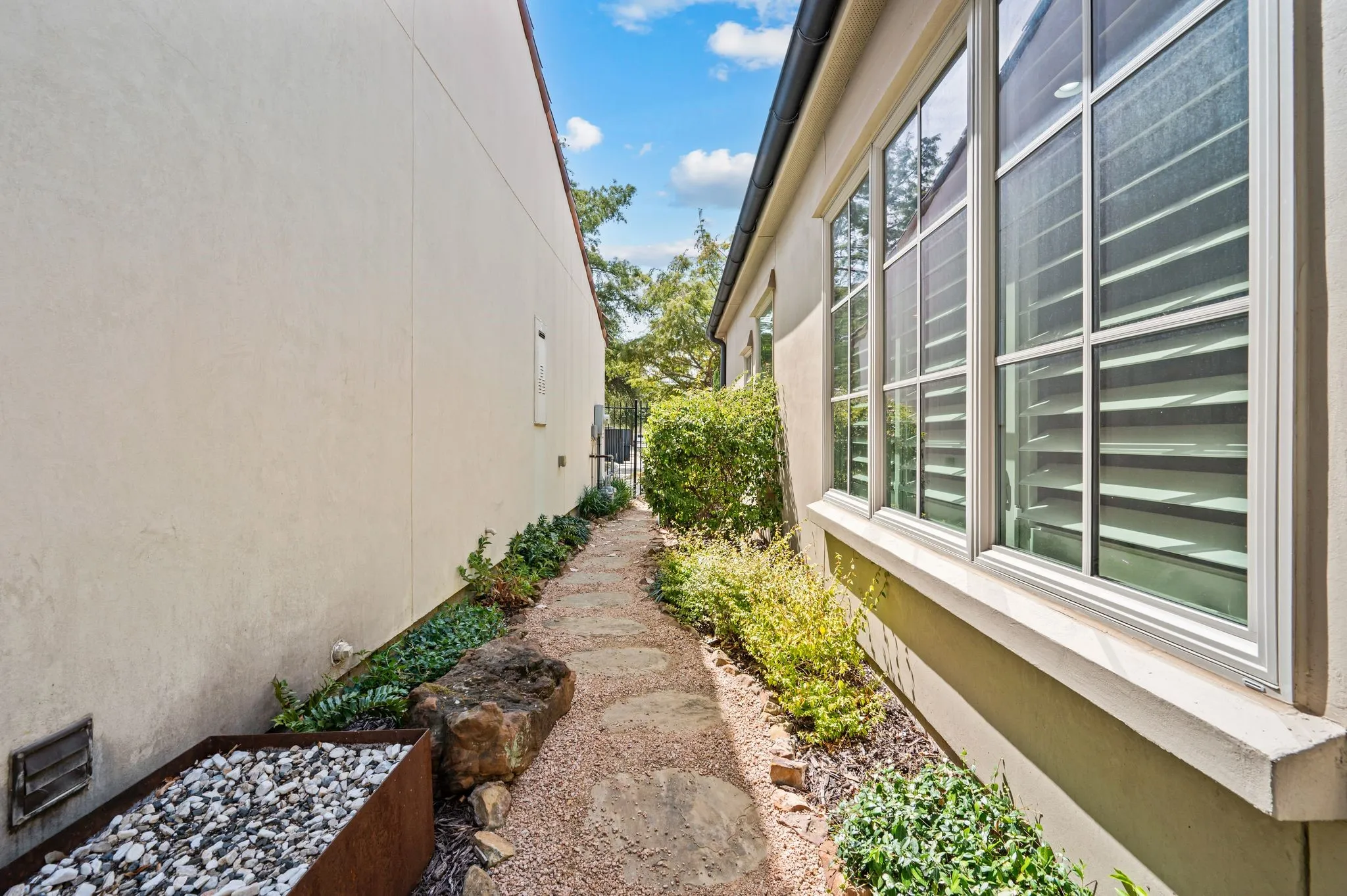 Stucco exterior with multiple windows featuring plantation shutters, a stone pathway, and established landscaping