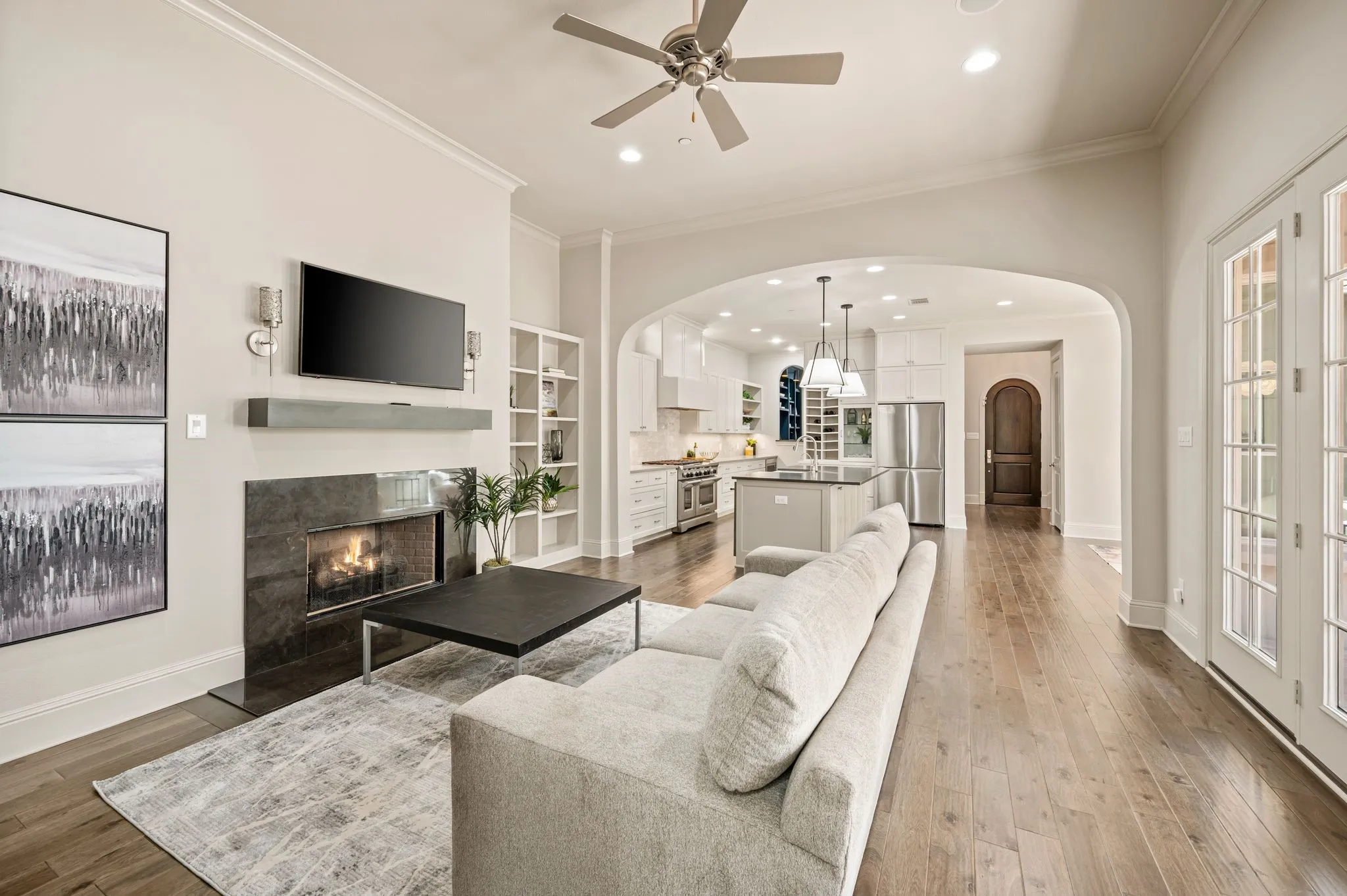 Hardwood flooring extends throughout this expansive living area, featuring a modern fireplace with a dark stone surround and a built-in shelving unit