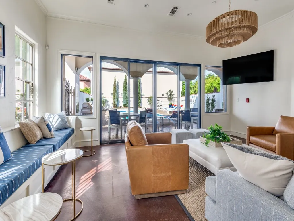 Spacious lounge area next to pool featuring a built-in window bench, large sliding glass doors, a wall-mounted television, and a tiered woven chandelier
