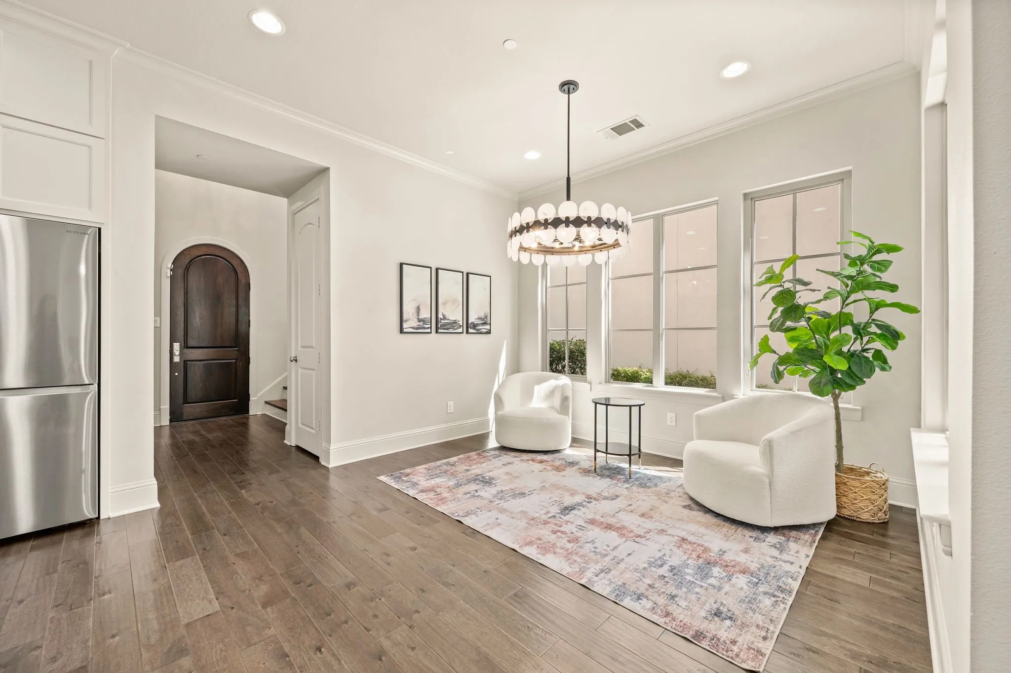 Wood-finish flooring throughout, stainless steel refrigerator, arched solid wood door, elegant chandelier, and expansive windows