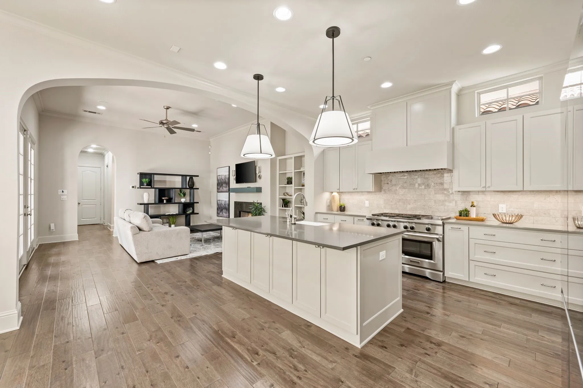 Gourmet kitchen featuring white cabinetry, a large center island with seating, stainless steel appliances including a gas range, pendant lighting, and quartz countertops