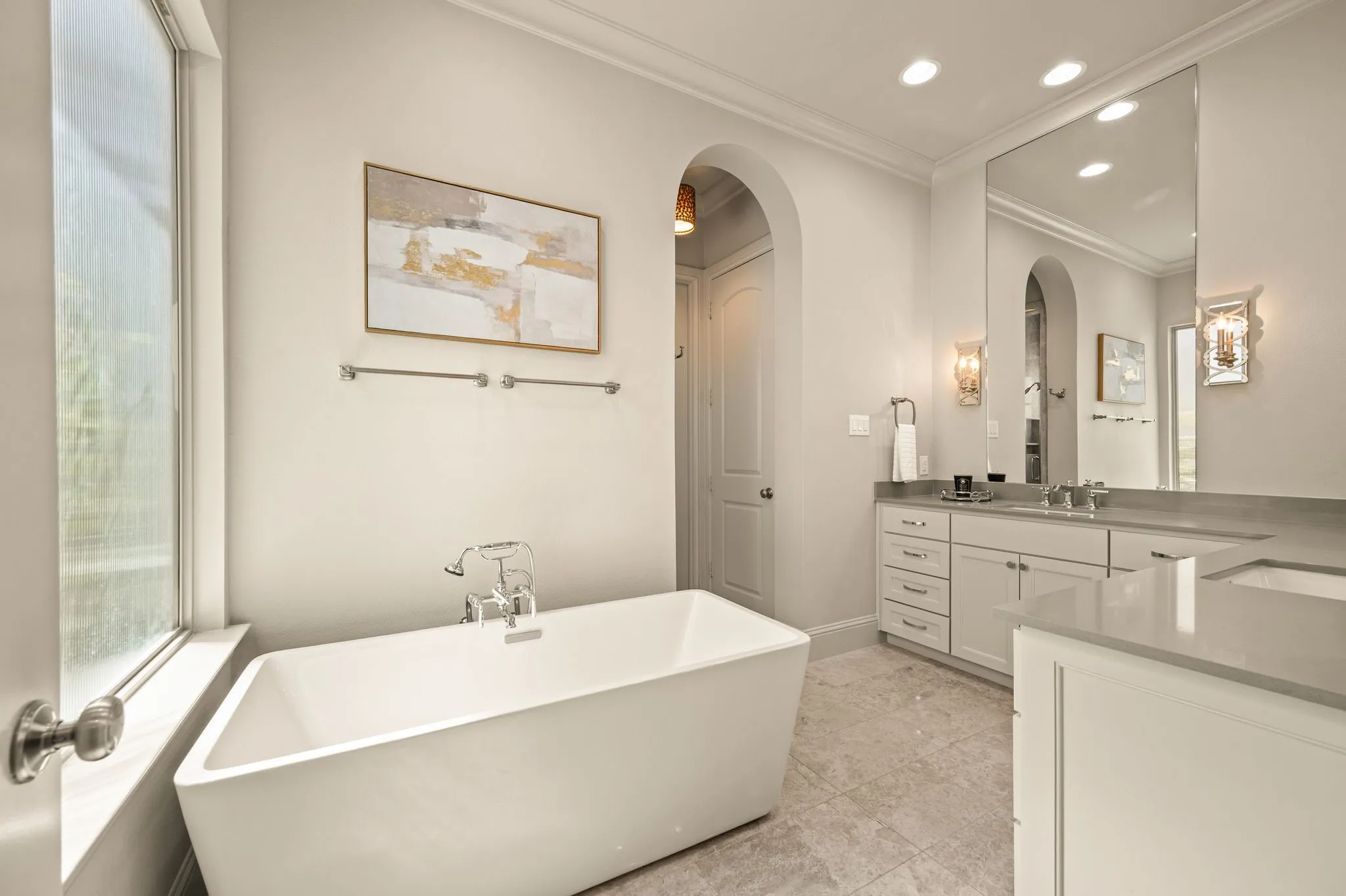 Freestanding soaking tub with chrome fixtures, dual vanity with undermount sinks, stone countertops, and recessed lighting