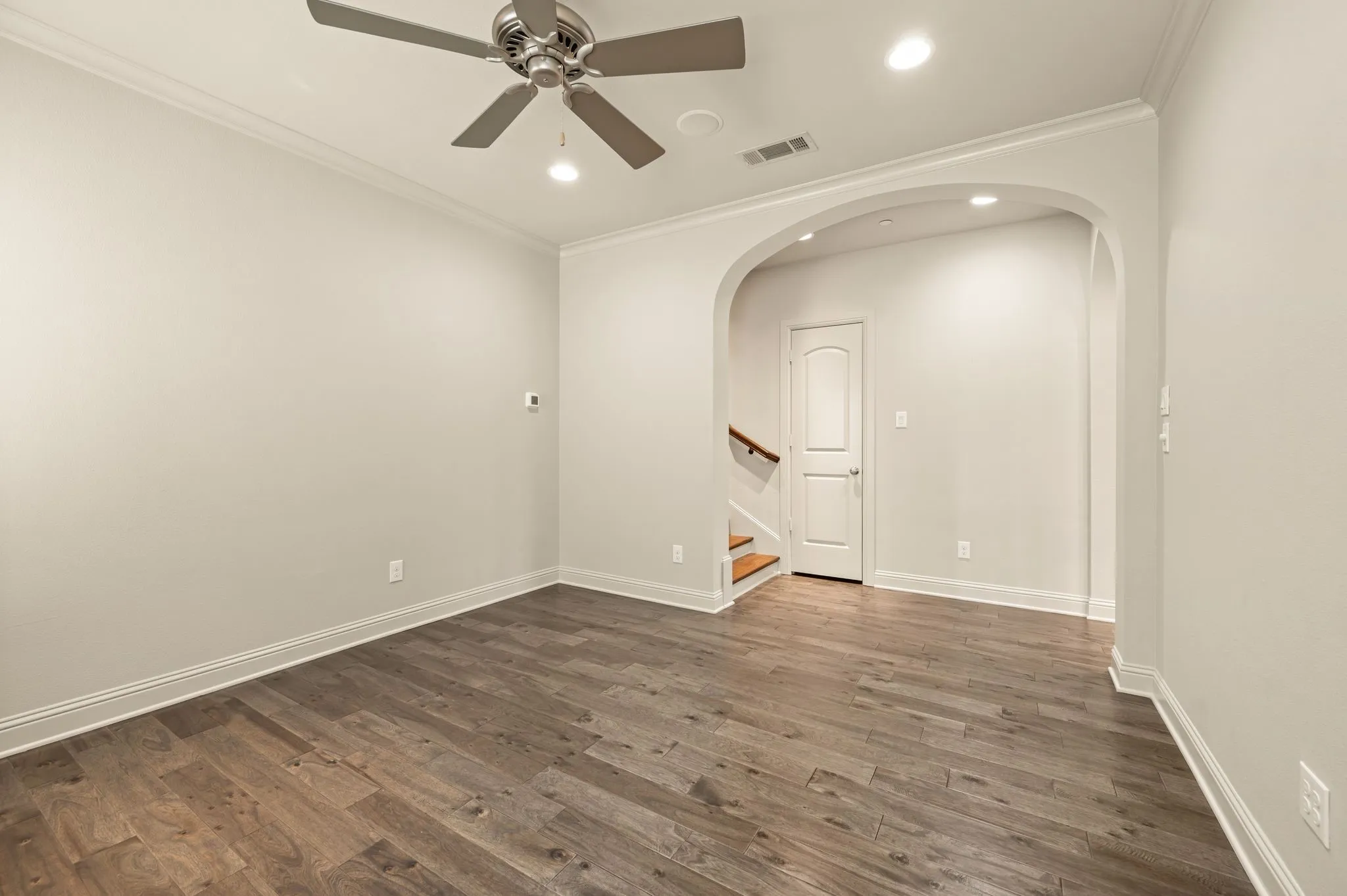 Wood-finish flooring with crisp white baseboards, crown molding, and recessed lighting