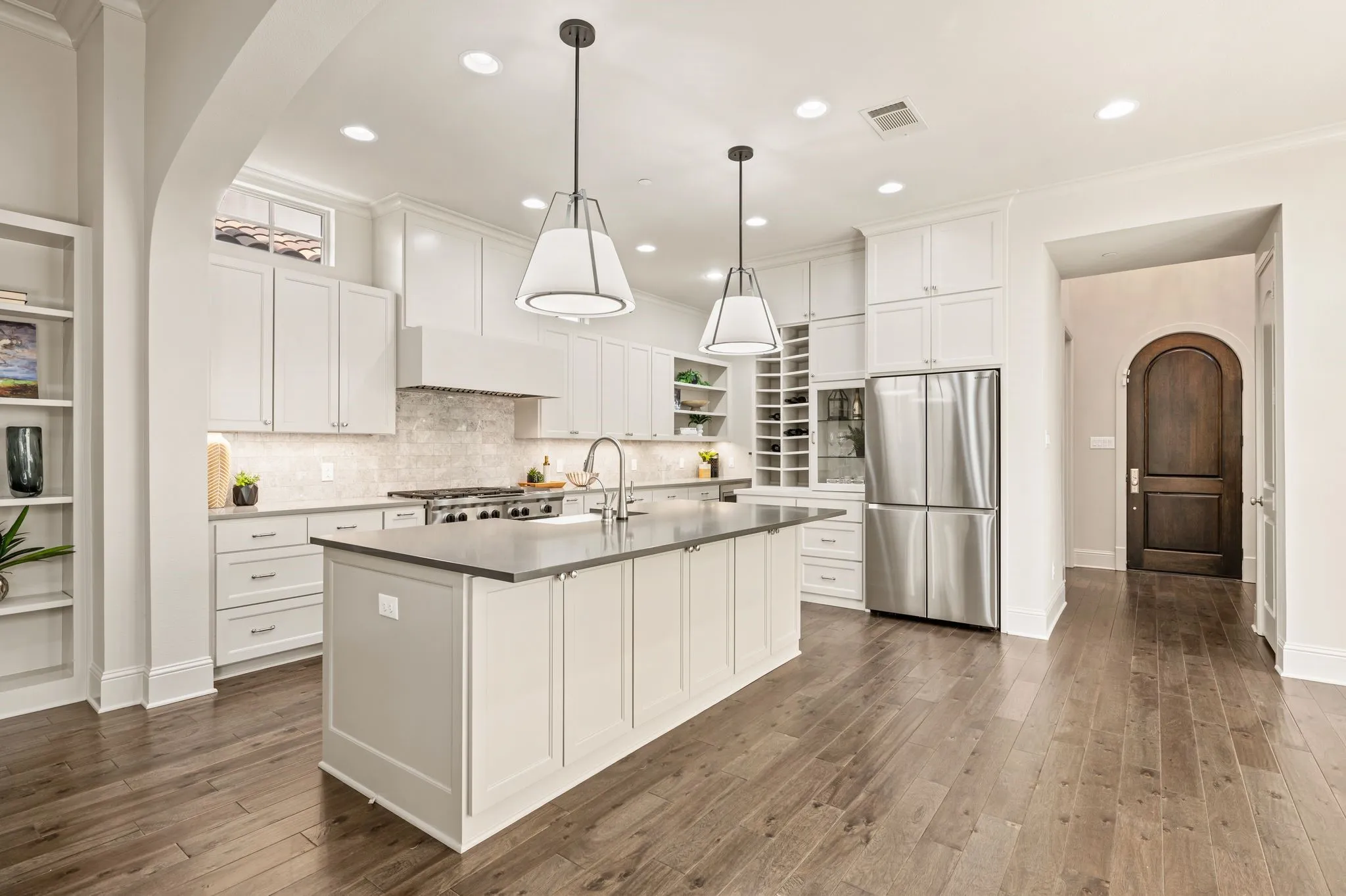 Gourmet kitchen featuring a large central island with sink, stainless steel appliances, recessed lighting, and white shaker cabinetry
