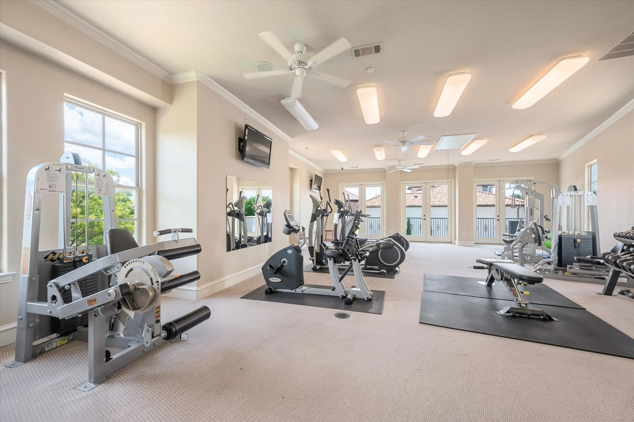 Spacious exercise room featuring multiple windows, French doors, recessed lighting, ceiling fans, and carpeted flooring