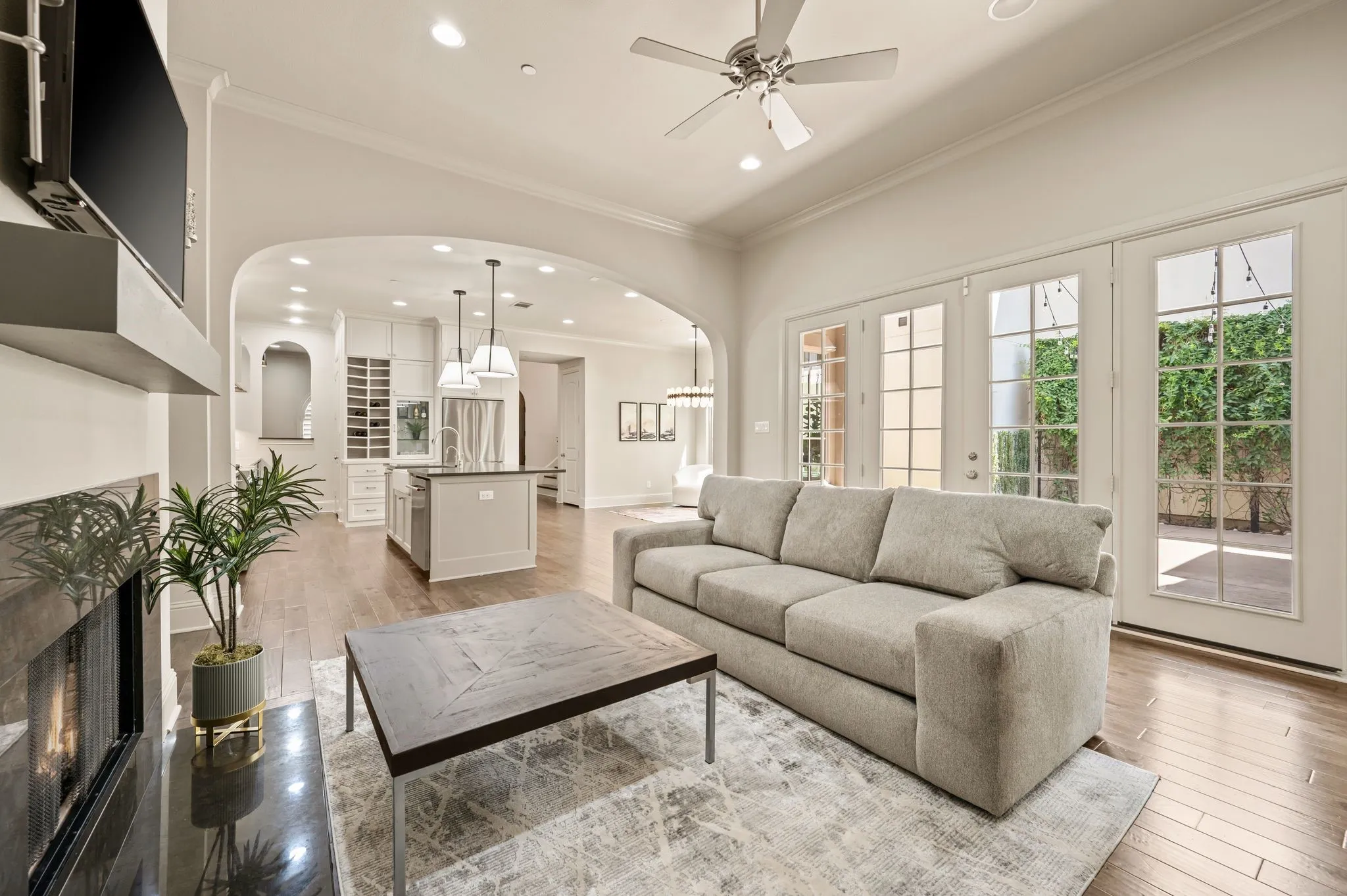 Recessed lighting, wood-finish flooring, and a ceiling fan are featured in this open-concept room with an arched entryway