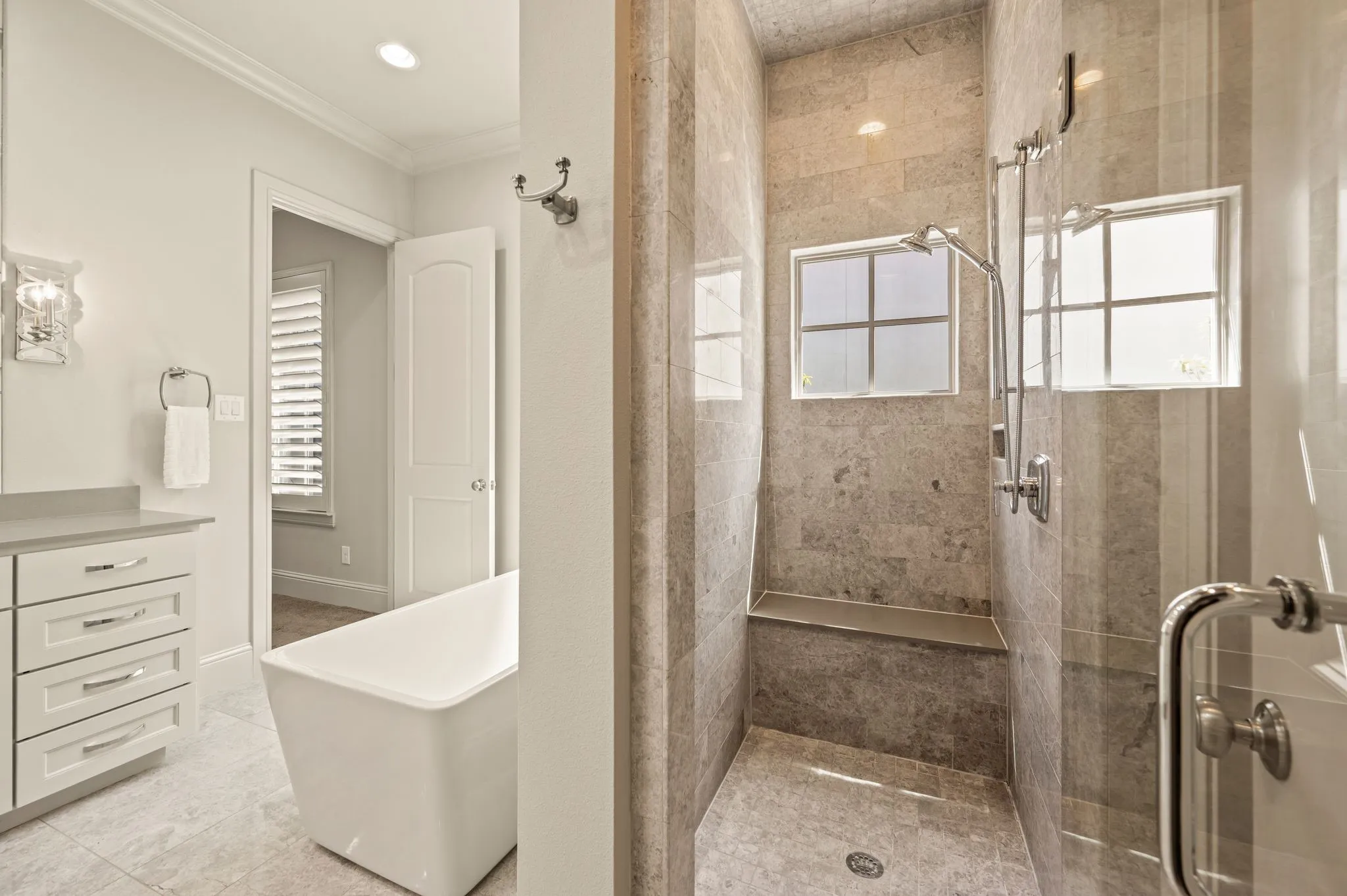 Freestanding soaking tub, walk-in shower with built-in bench, two showerheads, glass shower enclosure, and vanity with stone countertop