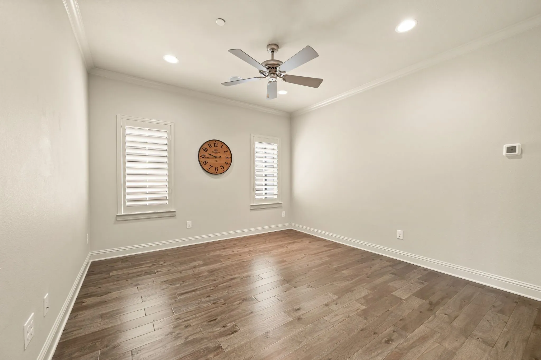Wood-finish flooring, two windows with louvered shutters, recessed lighting, and a ceiling fan with light