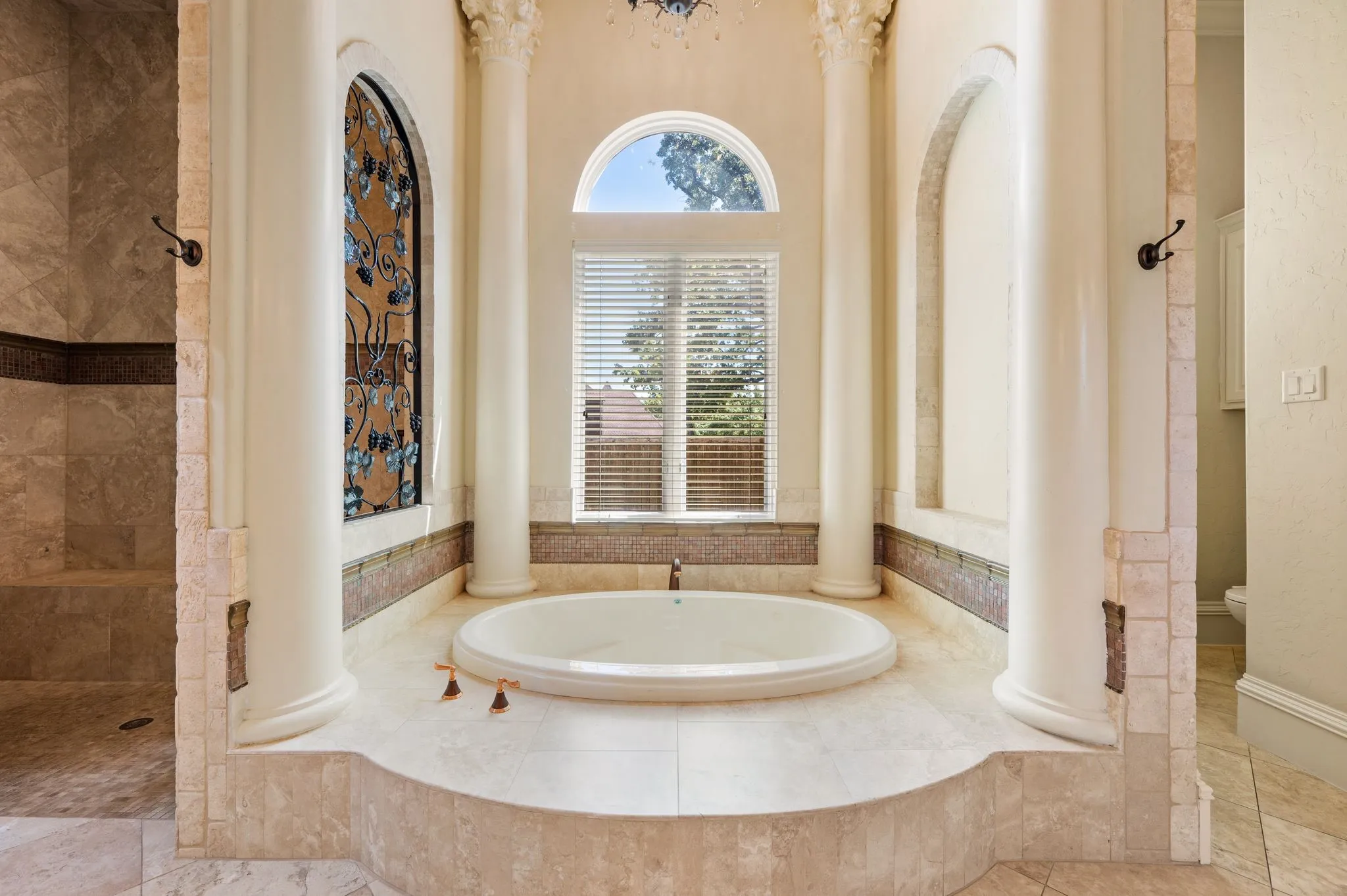 Built-in soaking tub with surrounding tile surround, arched window, decorative wall niche, and an adjacent walk-in shower with tiled walls