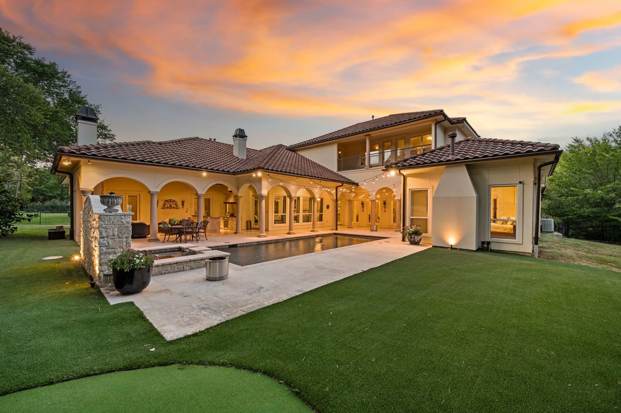 Expansive backyard featuring a rectangular swimming pool, stone patio, covered arched patio, and artificial turf lawn