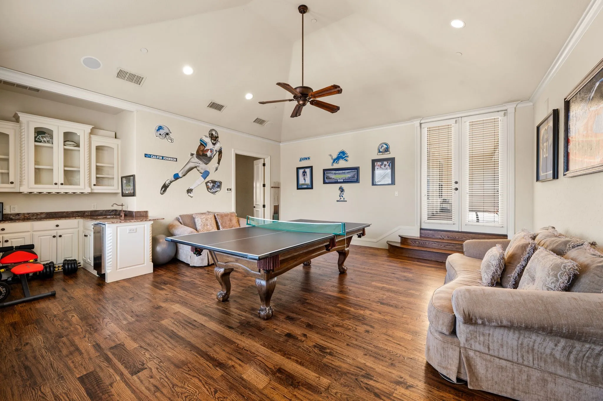 Vaulted ceiling with a ceiling fan, recessed lighting, wood-finish flooring, built-in cabinetry with glass-front uppers, and French doors