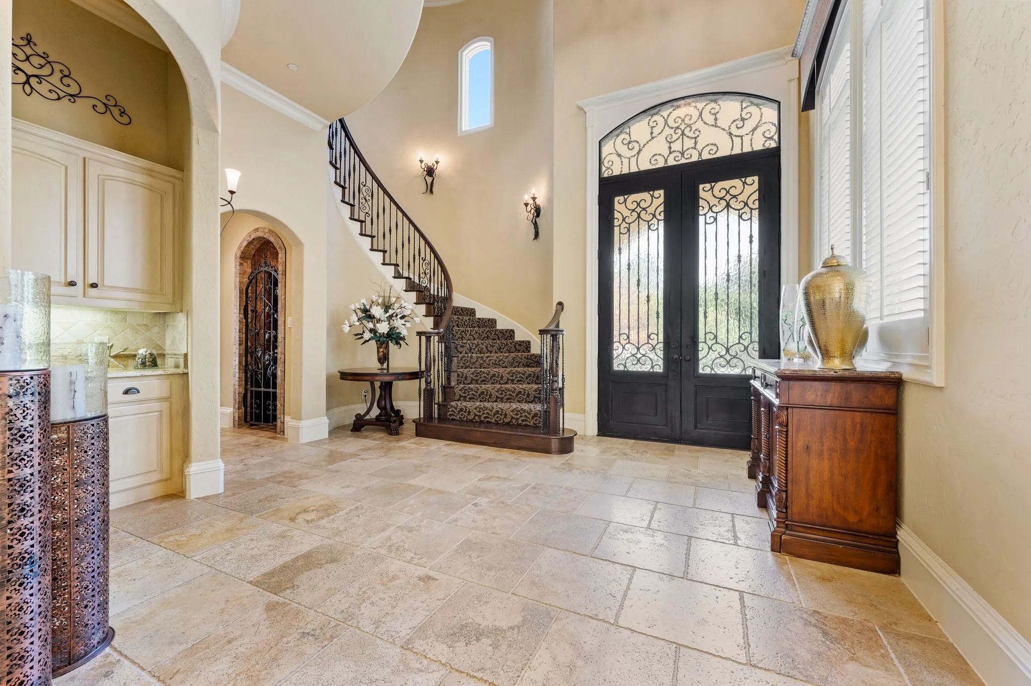 Two-story entryway featuring a curved staircase, wrought iron double doors, a built-in wet bar, and tile flooring