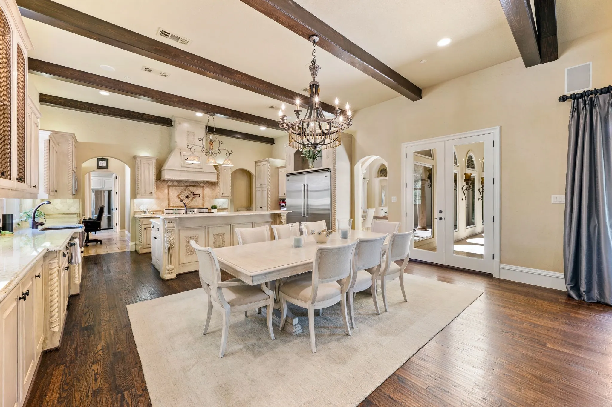 Hardwood flooring, exposed ceiling beams, built-in cabinetry, elegant chandelier, and double French doors