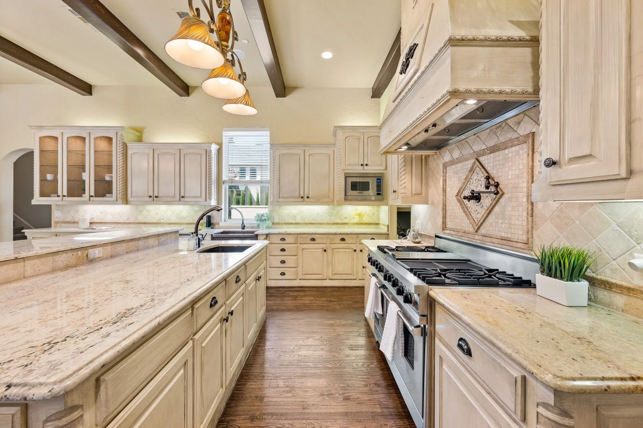 Chef's kitchen featuring custom cabinetry with glass-front upper cabinets, marble-finish countertops, a dual-fuel range with professional-grade hood, and a large center island with additional prep space