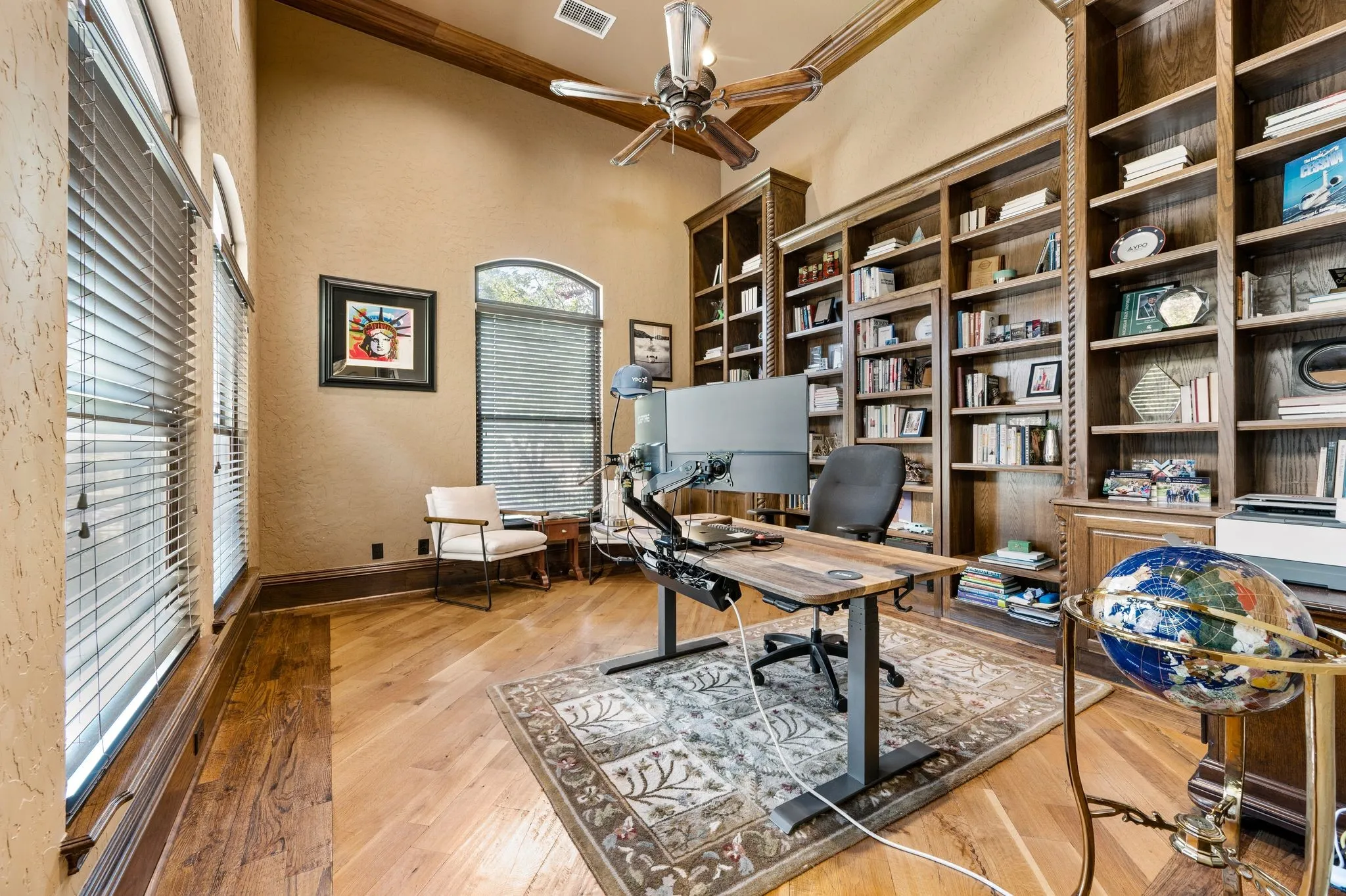 Hardwood flooring, vaulted ceiling with exposed wood beams, multiple windows with blinds, and extensive built-in cabinetry with shelving