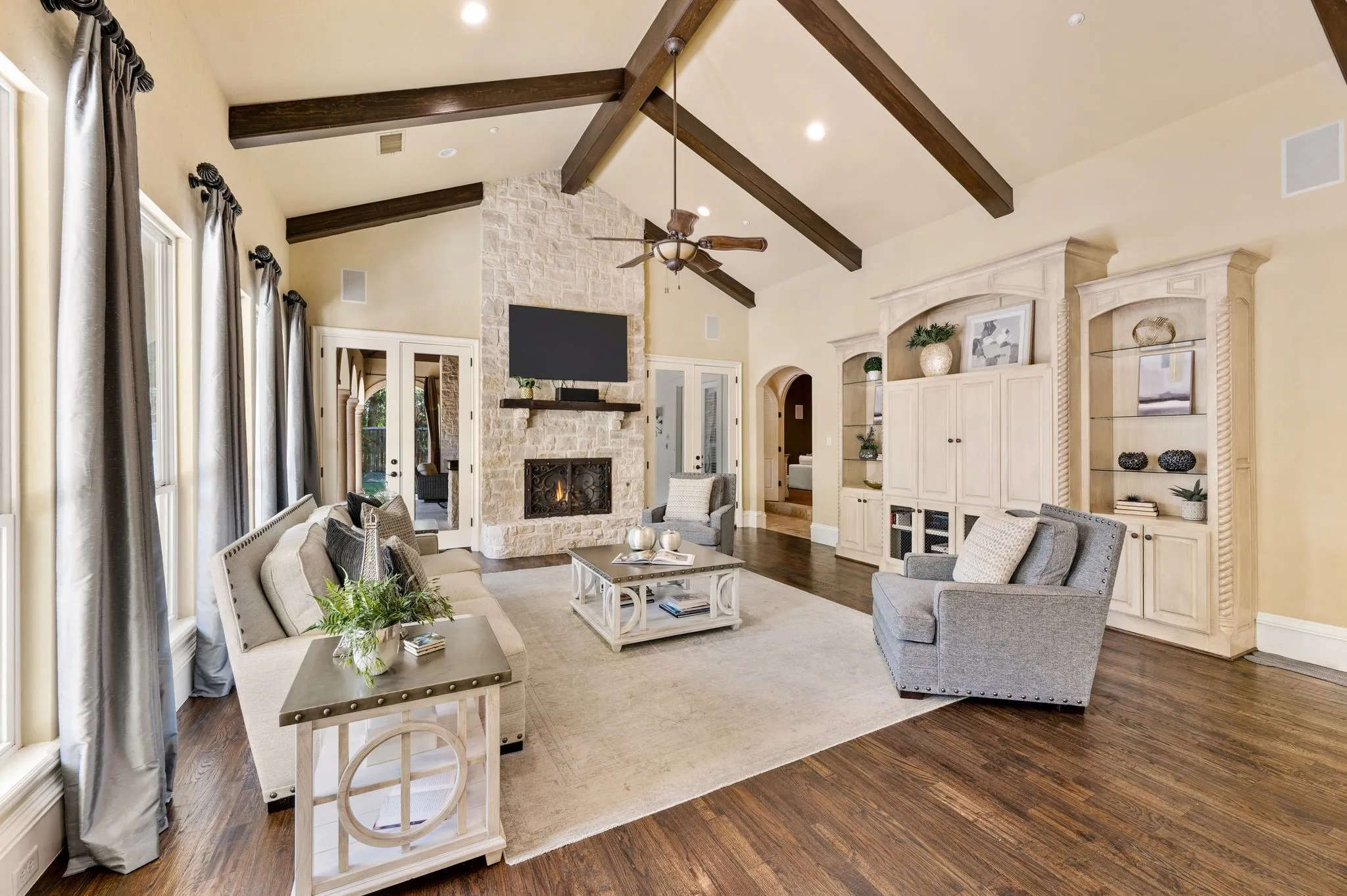 Vaulted ceilings with exposed beams, stone-clad fireplace, built-in entertainment cabinetry, dark wood-finish flooring, and recessed lighting