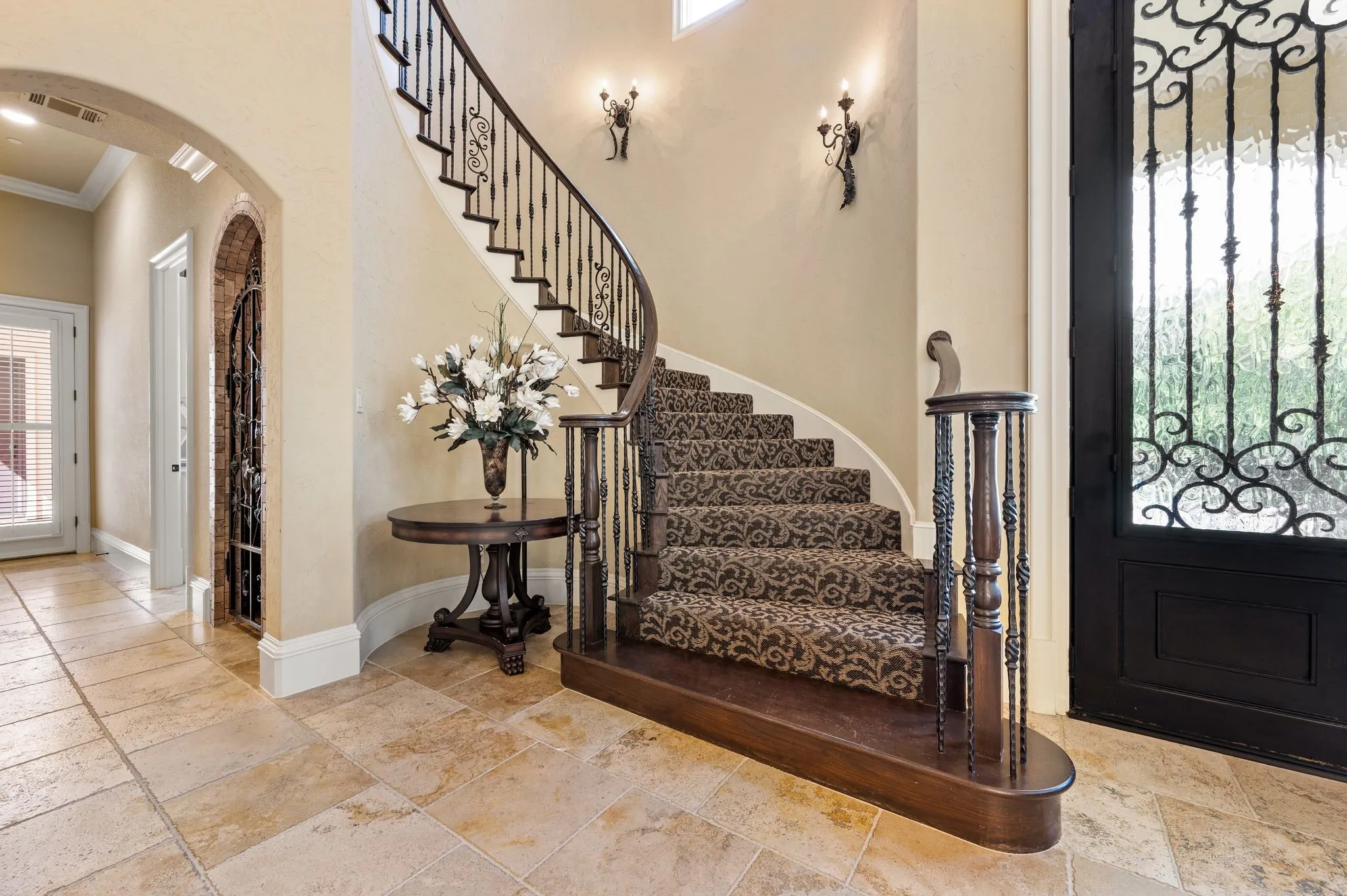 A curved staircase with wrought iron balusters, patterned stair runner leads to the second floor.