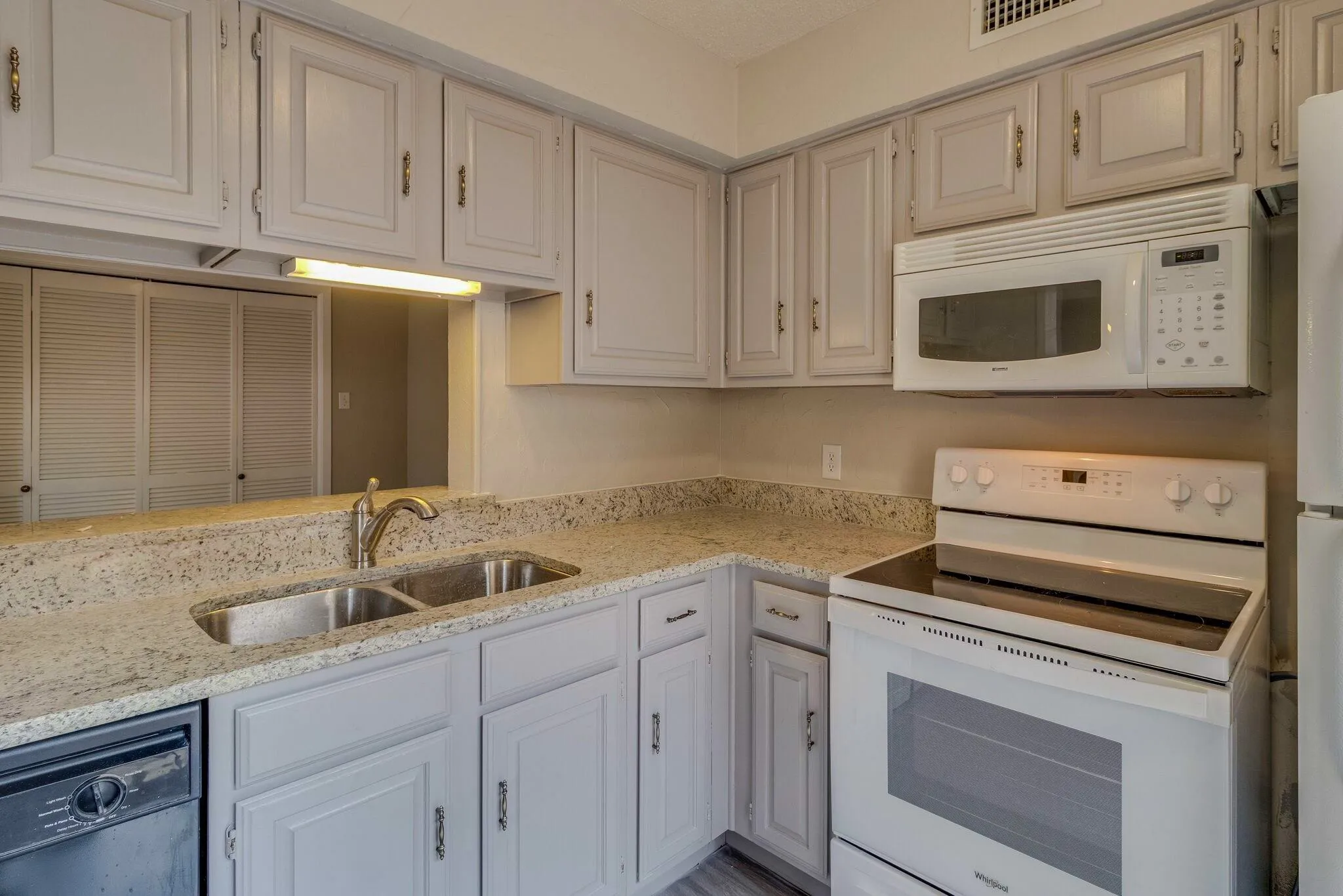 Kitchen featuring light gray cabinetry, light-toned countertops, a double basin stainless steel sink with a gooseneck faucet, and white appliances