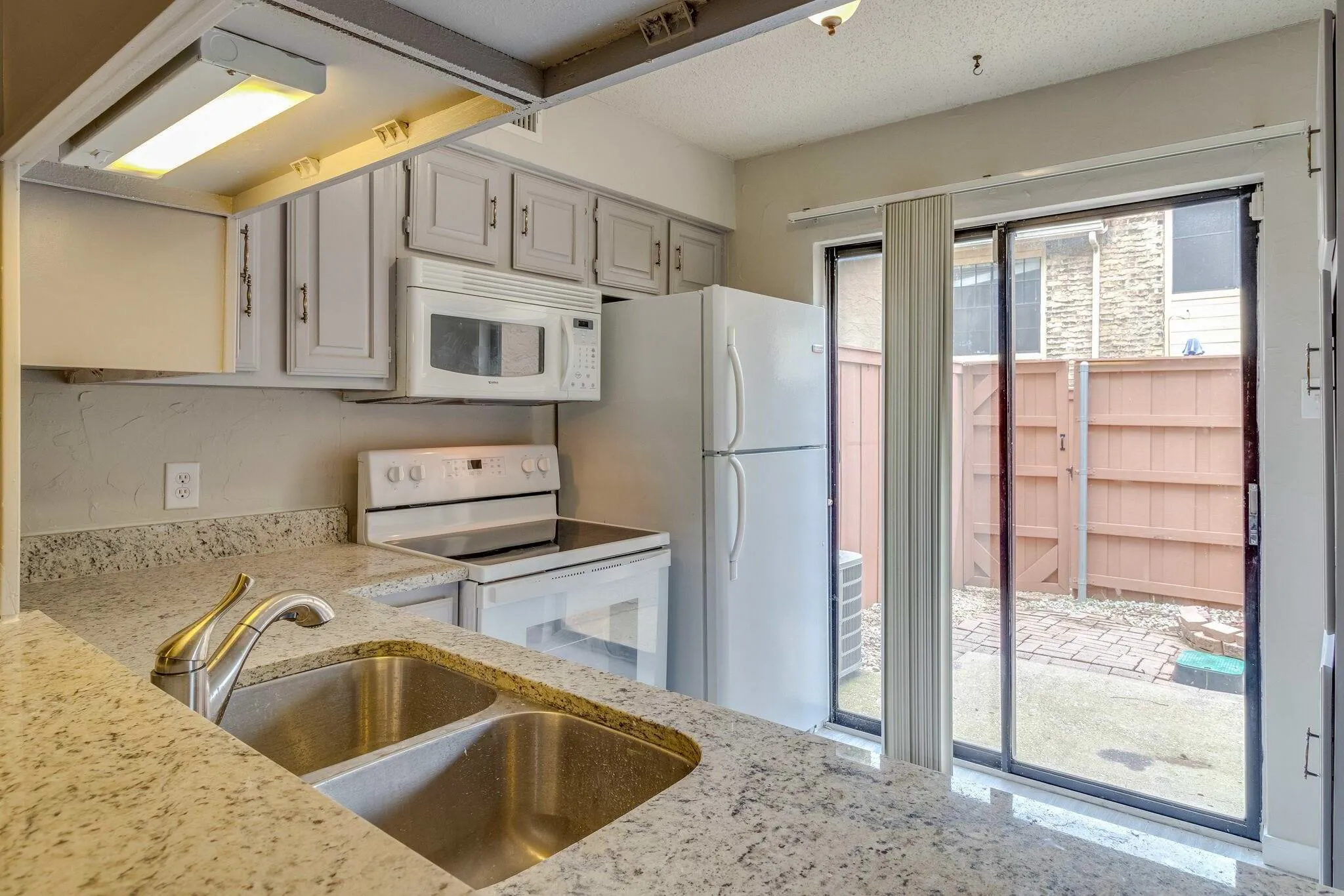 Kitchen featuring a double basin stainless steel sink, light-toned countertop, and light-painted cabinetry