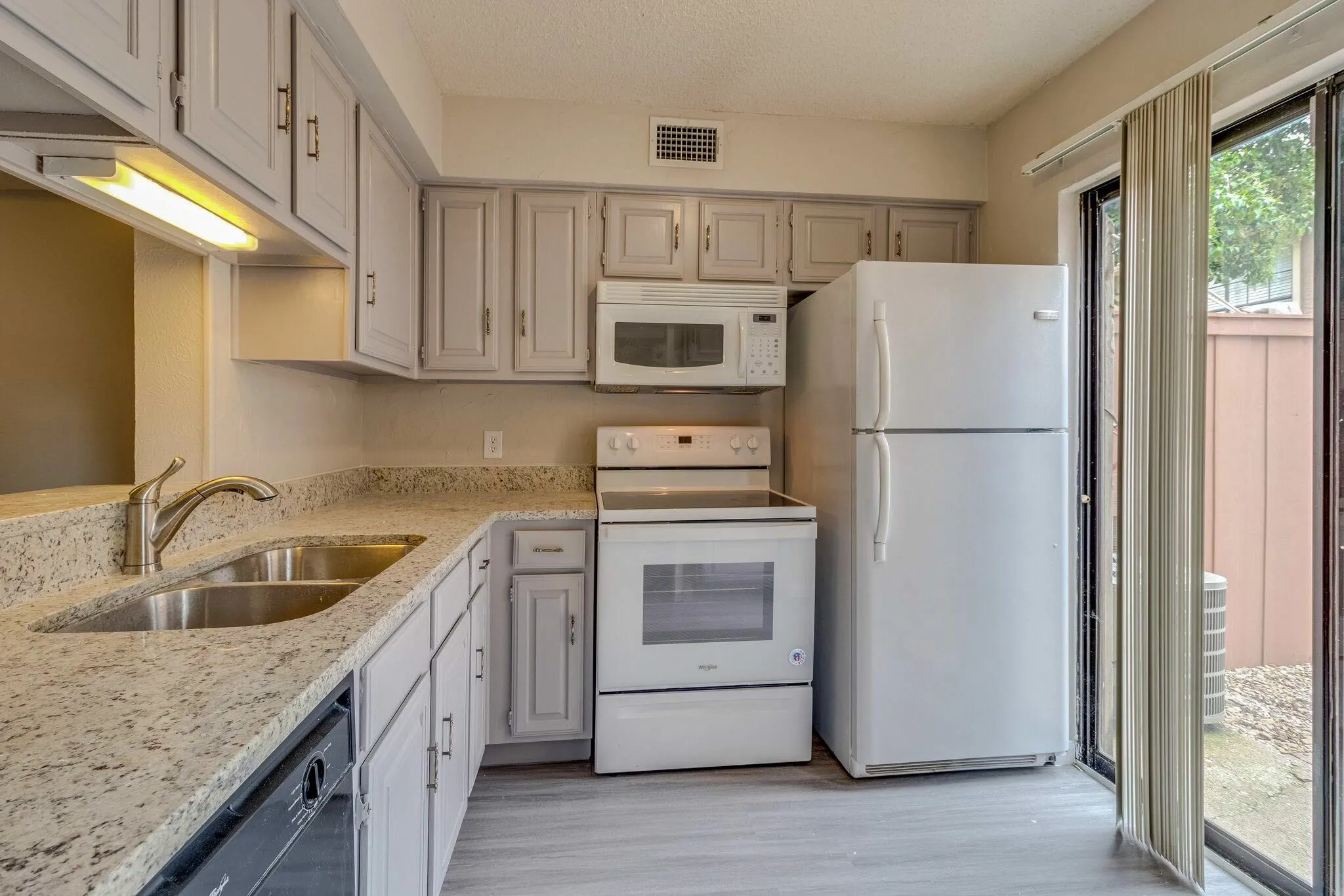 Kitchen featuring a double basin stainless steel sink, light-colored countertops, wood-finish flooring, white appliances, and light cabinetry