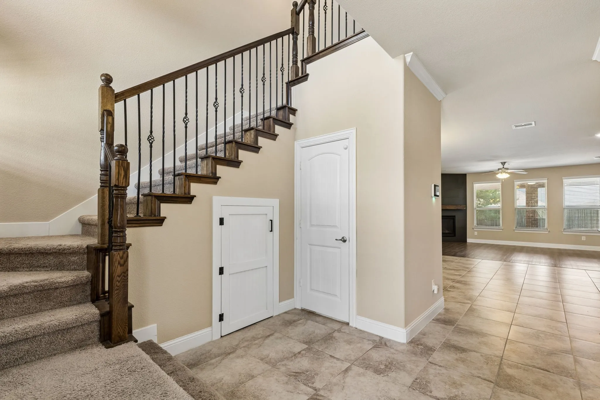 Carpeted staircase with wood newel posts and wrought iron balusters, tiled flooring, wood-finish flooring, and a ceiling fan with integrated lighting